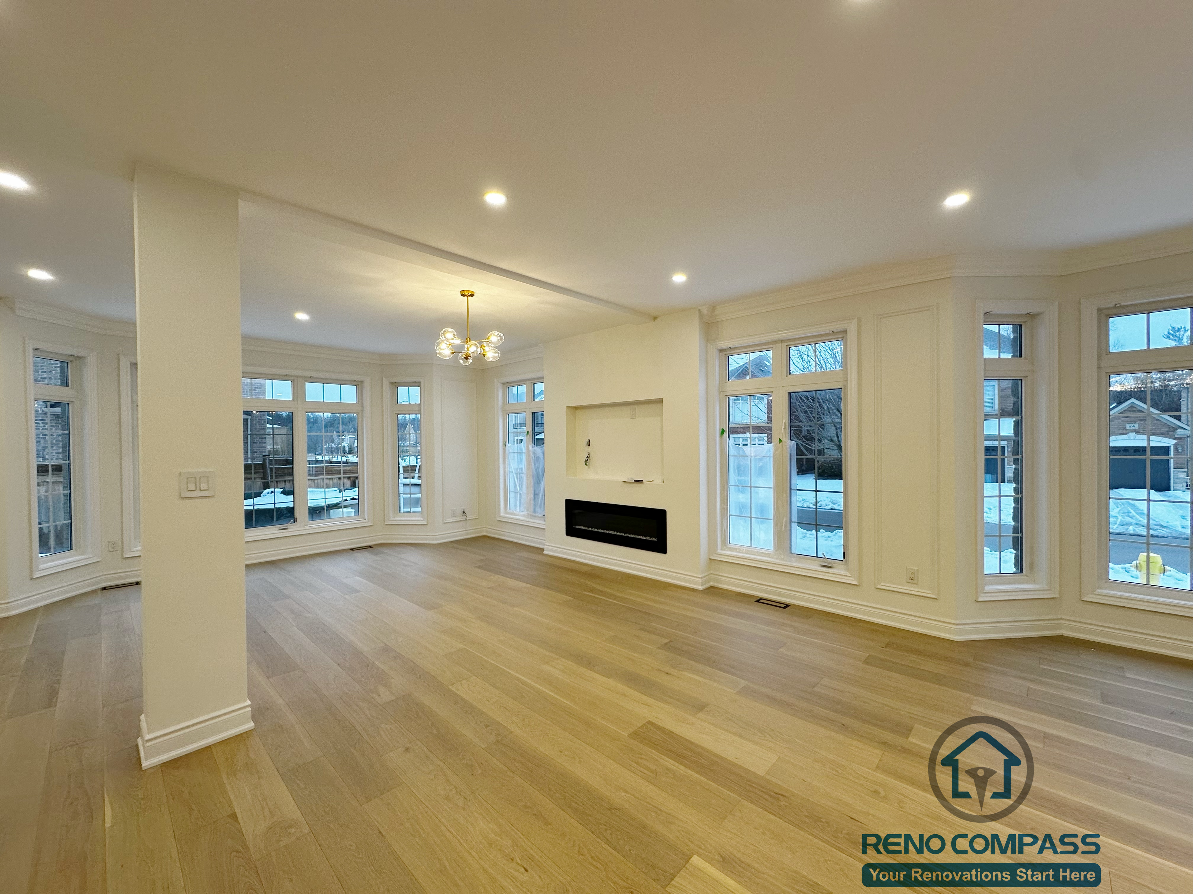 Open and airy living room completed as part of a Vaughan interior renovation, featuring wide-plank hardwood flooring, recessed ceiling lights, a modern built-in fireplace, and large surrounding windows that maximize natural light. The open layout and refined finishes reflect the craftsmanship of a professional Toronto renovation company.