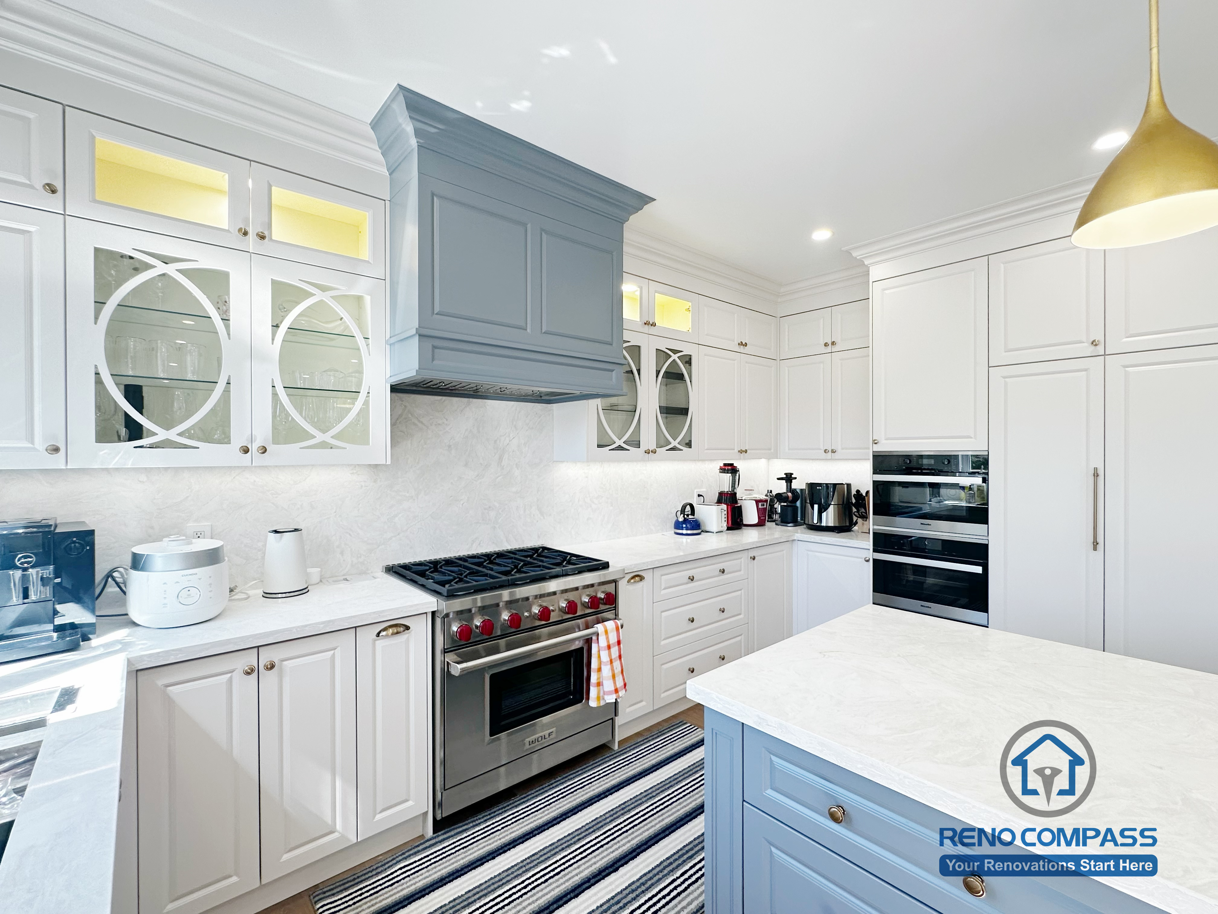 This North York kitchen renovation focuses on the cooking zone, featuring a custom-painted range hood, professional gas stove, quartz backsplash, and detailed shaker cabinetry with glass inserts. Thoughtful lighting and precise cabinetry alignment enhance both functionality and visual balance, reflecting Reno Compass’s attention to detail and craftsmanship.
