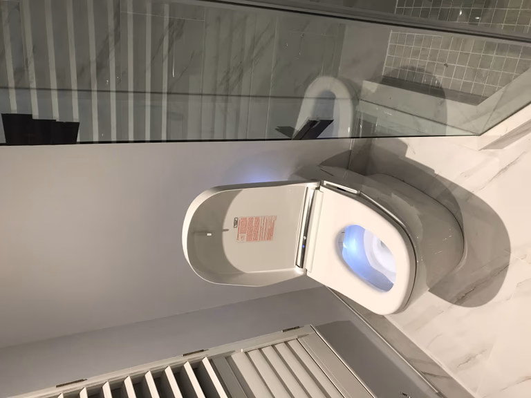 Contemporary Toronto bathroom renovation featuring a smart bidet toilet with LED lighting, sleek glass shower enclosure, large format marble tiles, and warm ambient lighting for a high-end, modern finish.