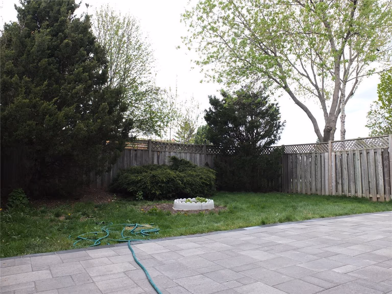 A completed backyard landscaping project in Mississauga featuring a newly installed interlocking stone patio, green lawn area, and decorative garden bed. The grey patio pavers create a clean and durable outdoor space while the surrounding landscaping adds natural balance to the backyard design. Completed by a professional Toronto Renovation Company, Reno Compass Inc., specializing in interlocking patios, landscaping, and exterior home upgrades across the GTA.