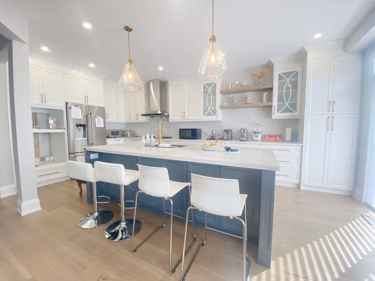 A spacious open-concept kitchen completed as part of a Richmond Hill interior renovation. This kitchen renovation features a large central island with seating, quartz countertops, custom cabinetry, modern pendant lighting, and integrated stainless steel appliances.
