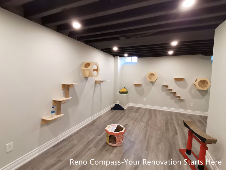 This Vaughan basement renovation features an extended cat climbing wall integrated into an industrial-style interior with a sprayed black open ceiling and recessed lighting. Wall-mounted platforms and climbing elements are arranged along the length of the space, creating a continuous and engaging path for pets while maintaining a clean and organized layout. The durable flooring and neutral wall finishes support everyday use and easy maintenance. Designed and completed by Reno Compass, this renovation highlights thoughtful space planning that balances functionality, movement, and visual clarity in a compact basement environment.