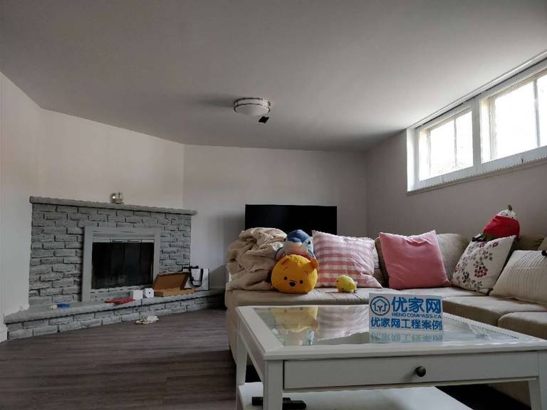 This Scarborough basement renovation showcases a comfortable finished living area featuring modern vinyl flooring, freshly painted walls, and upgraded baseboards. The space is styled with a sofa and coffee table to create a cozy lounge area, while the basement window allows natural light to brighten the room. This functional design transforms the basement into a welcoming relaxation space perfect for family gatherings or everyday living.