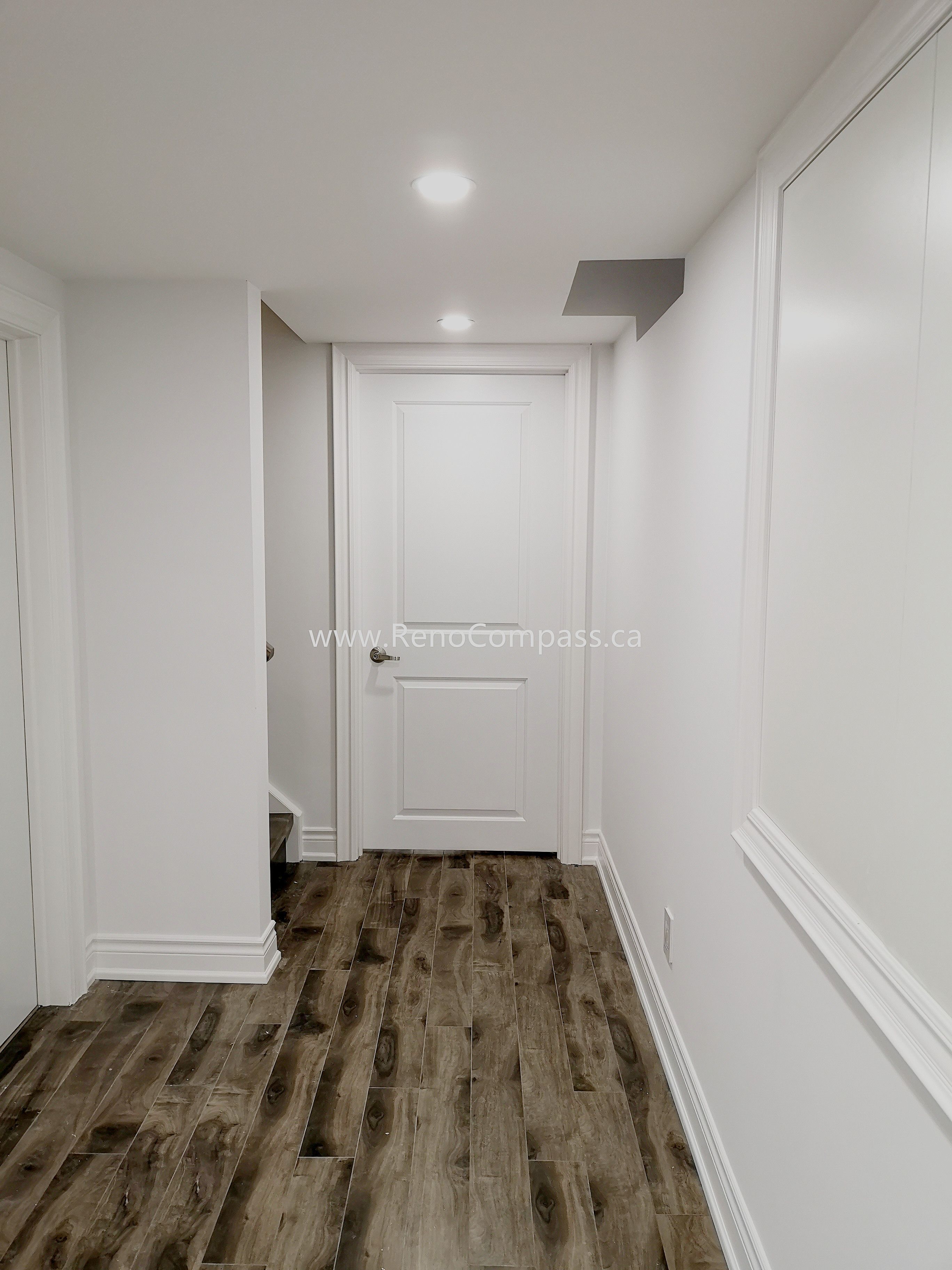 This Vaughan basement renovation features a clean and modern hallway design with durable wood-style flooring, smooth white walls, and recessed ceiling lighting for a bright and welcoming atmosphere. The upgraded basement corridor enhances overall flow and accessibility while maintaining a contemporary finish throughout the space. Completed by Reno Compass Inc., this renovation showcases quality craftsmanship and thoughtful design, creating a polished and functional basement living environment that complements the entire home renovation.