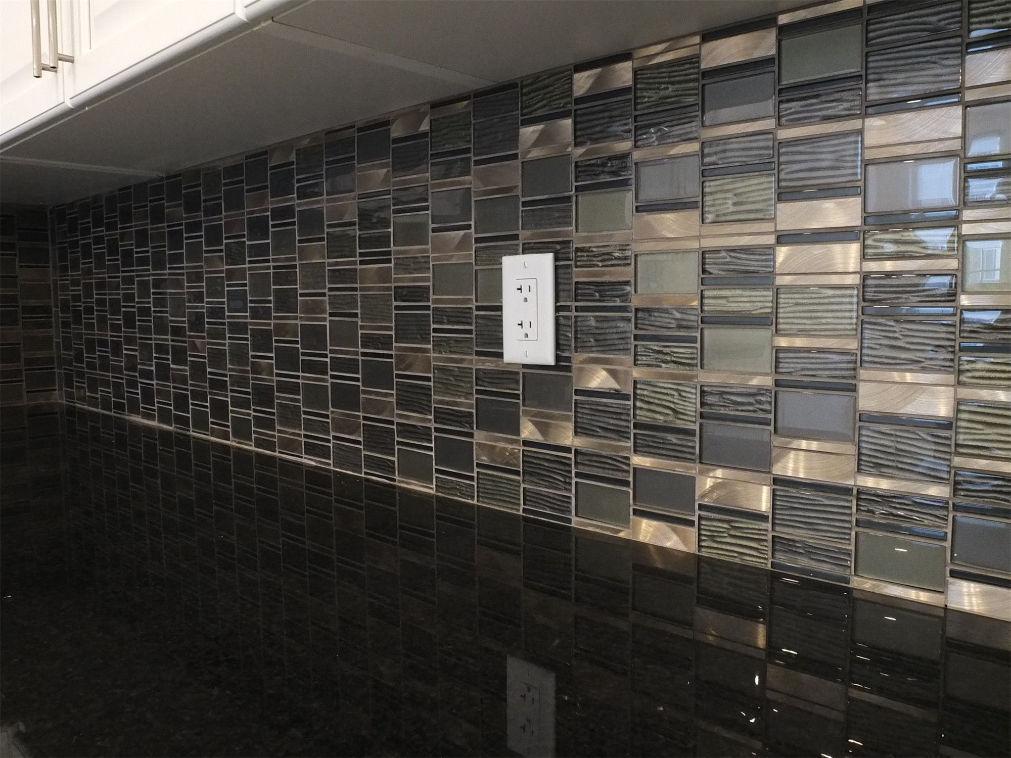 This Kleinburg interior renovation highlights a close-up view of the modern mosaic tile backsplash installed behind the kitchen countertop. The combination of glass and textured tiles in dark tones creates a stylish contrast against the sleek black countertop and white cabinetry. Precision tile installation enhances both durability and visual depth, adding a sophisticated finishing detail to the contemporary kitchen design.
