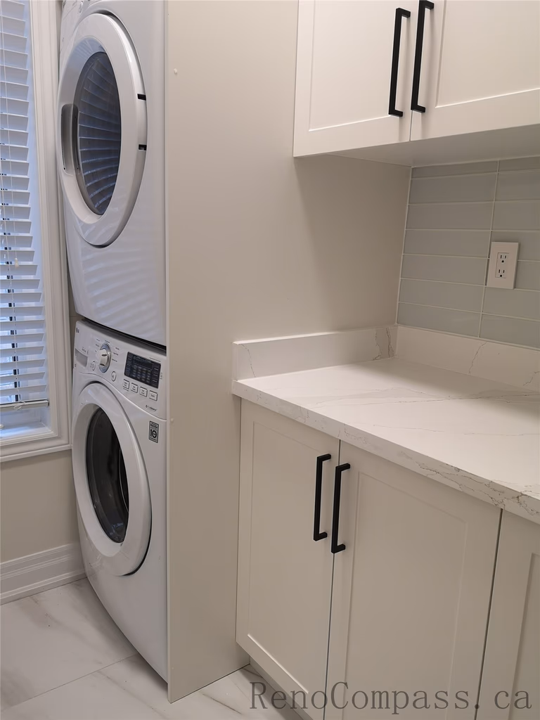 This Aurora interior renovation features a modern laundry room with custom white shaker cabinets, quartz countertop, and integrated utility sink with matte black faucet. The stacked washer and dryer design maximizes space while maintaining a clean and functional layout. Completed by a professional Toronto renovation company focused on efficient storage solutions, modern finishes, and high-quality craftsmanship for everyday living.