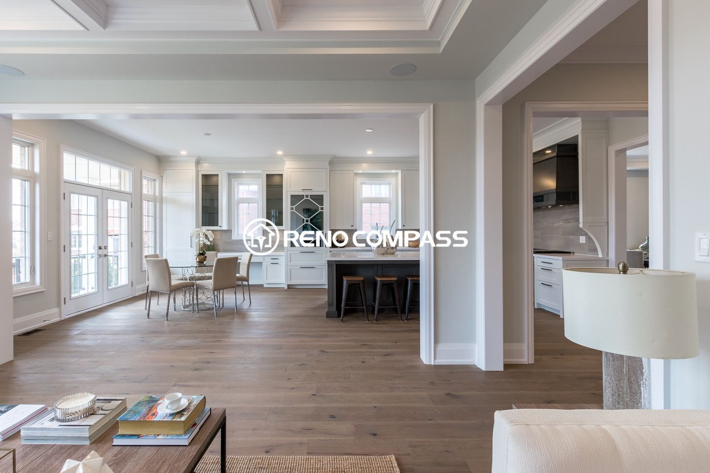 Bright open-concept kitchen and dining area renovation in Newmarket featuring custom white cabinetry, large windows, modern glass dining table, and engineered hardwood flooring. The design creates a spacious and elegant living environment that seamlessly connects the kitchen, dining, and outdoor access areas.