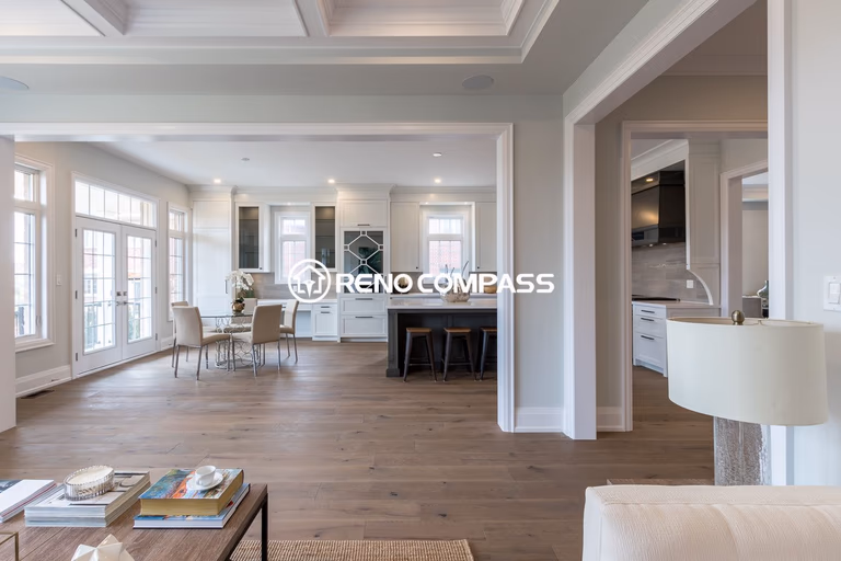 Bright open-concept kitchen and dining area renovation in Newmarket featuring custom white cabinetry, large windows, modern glass dining table, and engineered hardwood flooring. The design creates a spacious and elegant living environment that seamlessly connects the kitchen, dining, and outdoor access areas.
