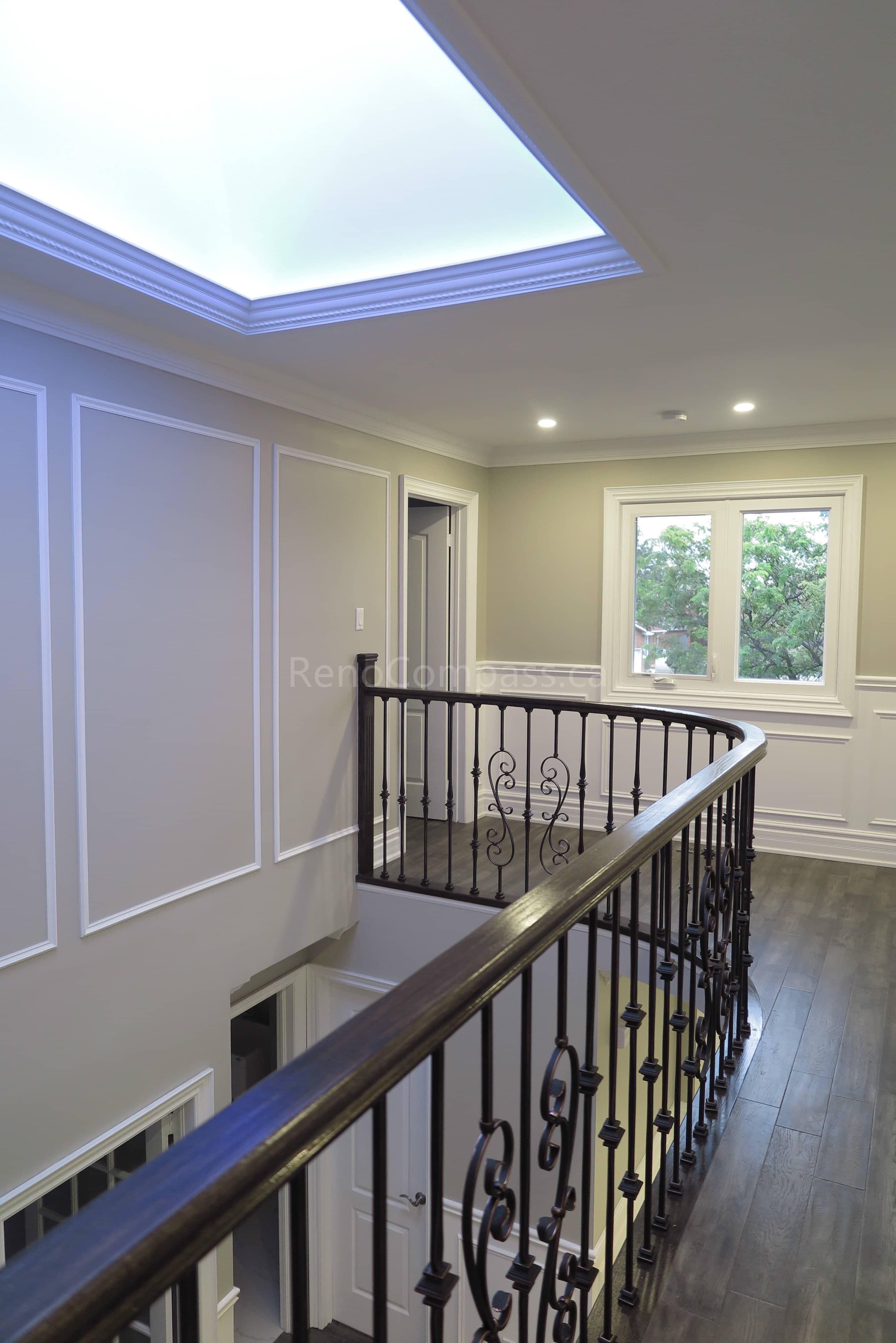 This Markham interior renovation showcases an elegant upper hallway and staircase area featuring custom wrought iron railings, detailed wall panel molding, and modern hardwood flooring. The space is enhanced by recessed lighting and a contemporary tray ceiling with soft ambient illumination, creating a bright and refined transition between levels. Completed by Reno Compass, a trusted renovation contractor specializing in custom interior finishing and full home renovations across Markham and the Greater Toronto Area.