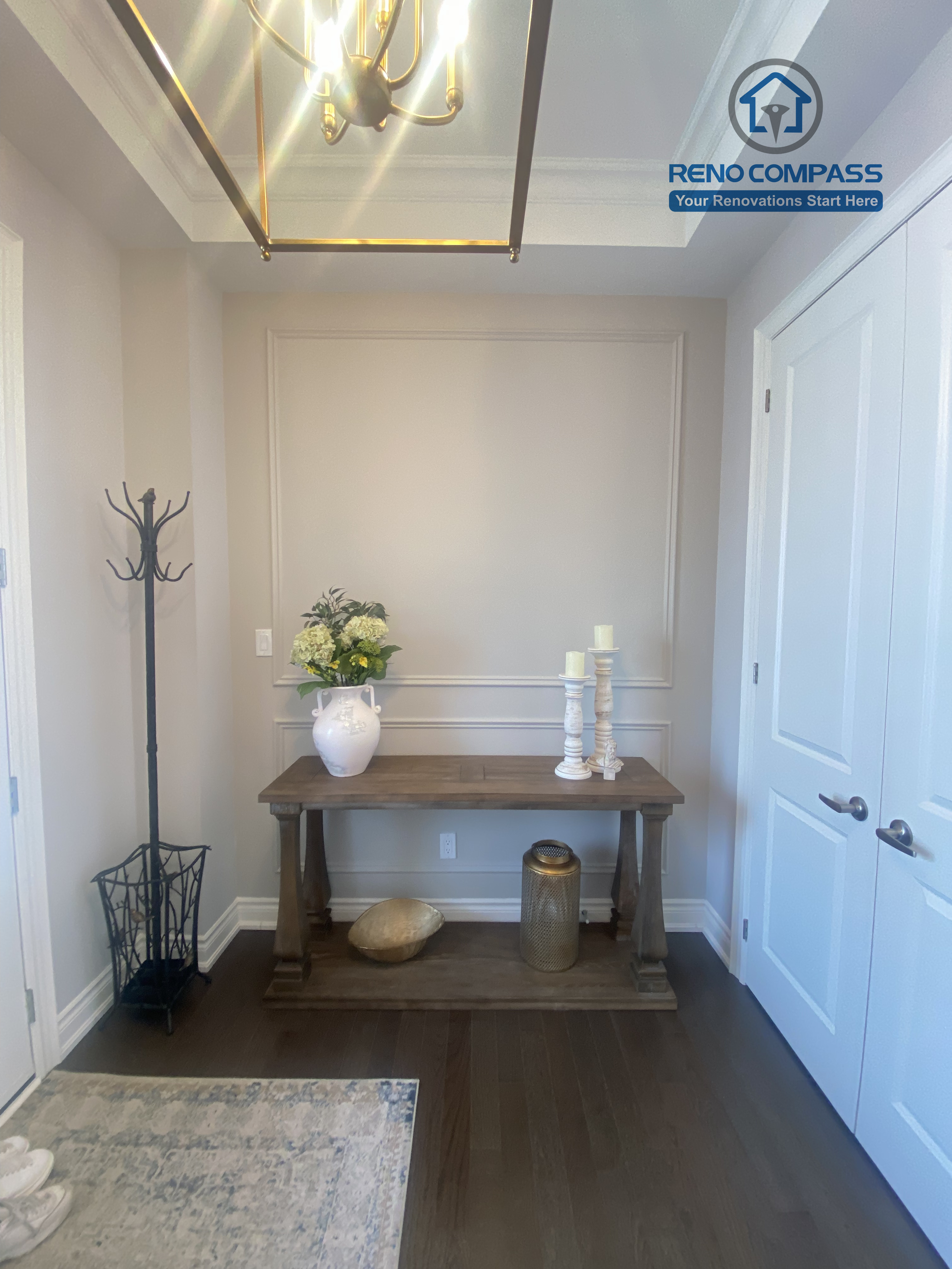 This Vaughan interior renovation showcases an elegant entryway with a feature chandelier, decorative console table, and clean wall panel detailing. Warm wood flooring and balanced proportions create a welcoming first impression, completed by a professional Toronto renovation company.
