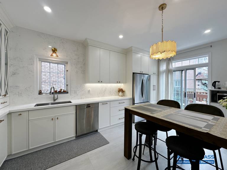This Markham kitchen renovation showcases a bright and well-balanced layout with custom white cabinetry, quartz countertops, and a functional dining island. A statement chandelier adds warmth and visual focus above the seating area, while integrated lighting enhances both task efficiency and overall ambiance. Large windows and patio doors allow natural light to flow through the space, creating a kitchen designed for everyday comfort, family dining, and seamless indoor-outdoor living.