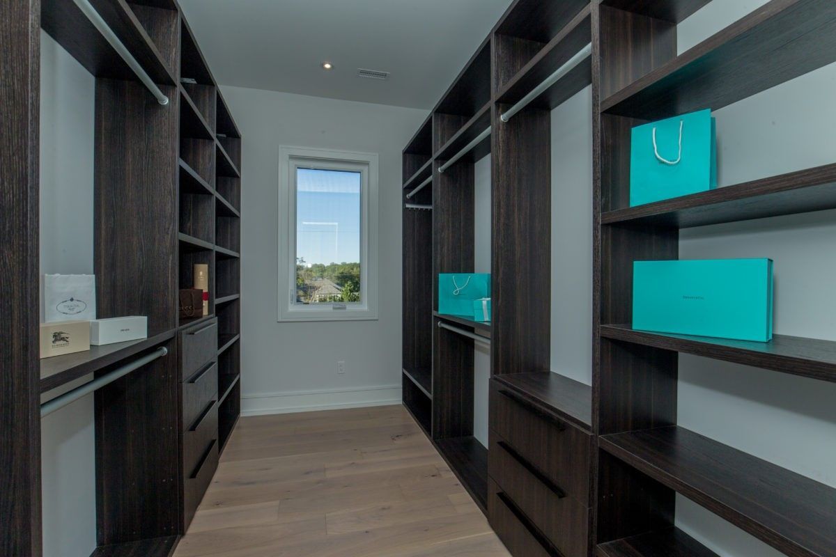 Luxury walk-in closet renovation in a 5000 sqft Toronto custom home featuring dark wood built-in shelving, full-height wardrobes, integrated drawers, and open display storage for organized dressing space. This modern closet design maximizes storage efficiency while maintaining a clean, high-end interior aesthetic with natural lighting and hardwood flooring. Completed by Reno Compass Inc., a professional Toronto renovation company specializing in custom interior renovations and luxury home upgrades.