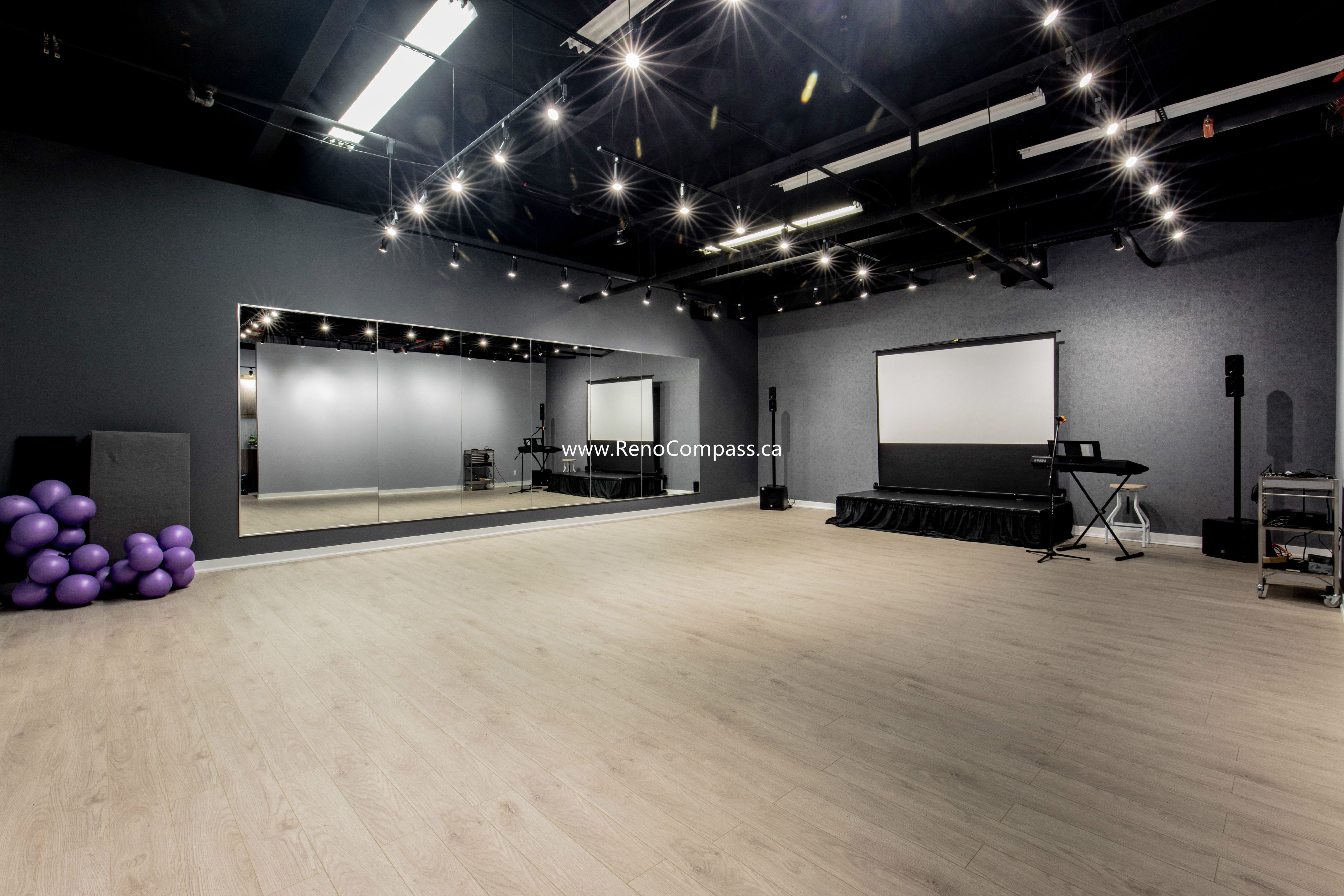 A spacious commercial studio renovation featuring luxury vinyl plank flooring, full-length mirrors, and professional track lighting. This Richmond Hill project showcases a modern industrial aesthetic with an exposed black ceiling, perfect for music schools and dance studios.