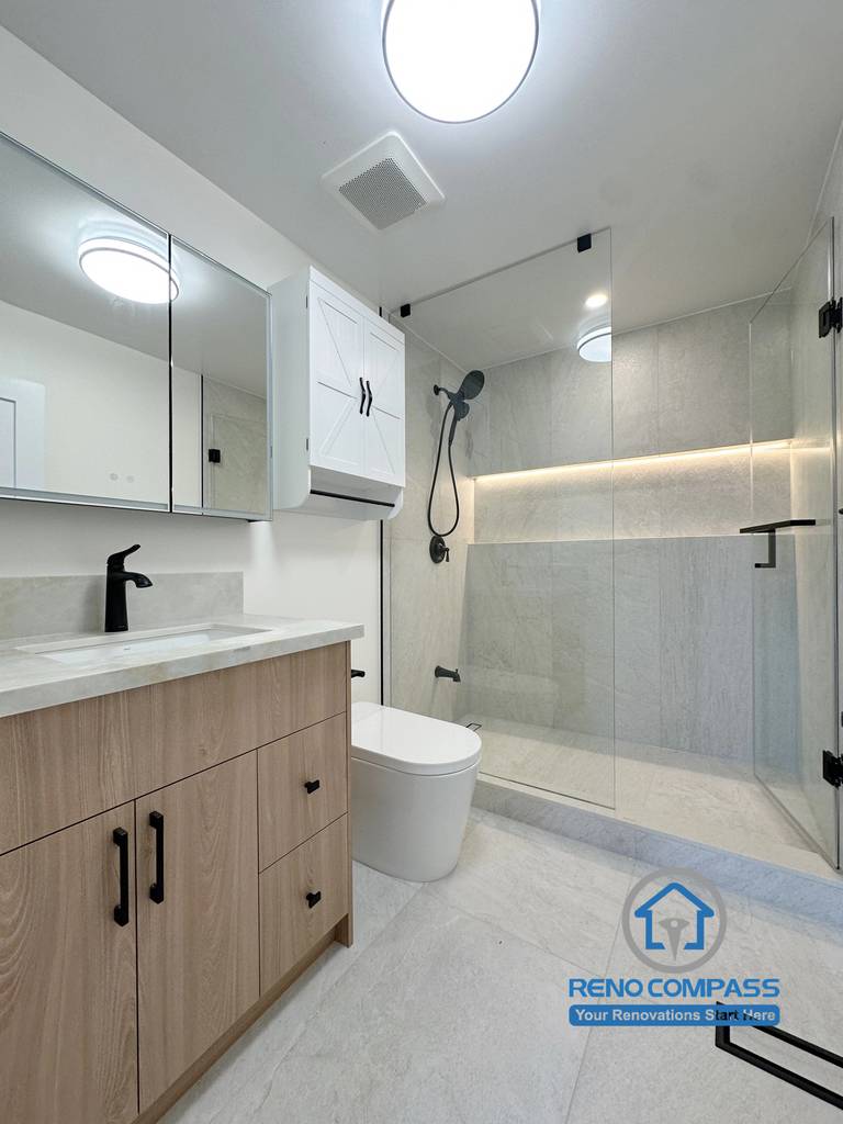A modern guest bathroom featuring a frameless glass walk-in shower, custom vanity with quartz countertop, matte black fixtures, illuminated shower niche, and large-format porcelain tile. Completed during a luxury whole home renovation in Markham, Ontario, this contemporary bathroom maximizes functionality, elegant design, and premium craftsmanship by Reno Compass.