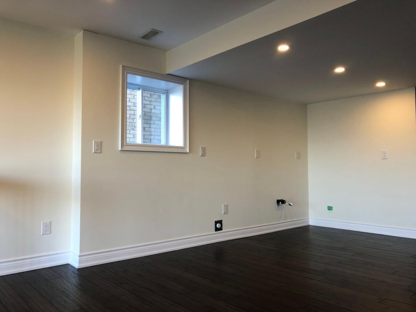 Spacious open-concept living area completed as part of a Toronto basement renovation project, featuring dark hardwood flooring, recessed pot lighting, smooth ceiling finish, and large window installation to maximize natural light in the lower level.