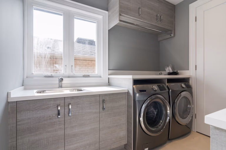 This custom-designed laundry room is part of a 4,500 sq ft luxury interior renovation in Toronto. Featuring built-in cabinetry, a quartz countertop with integrated utility sink, and a clean, functional layout, the space balances efficiency with contemporary aesthetics. The neutral color palette and organized storage system reflect thoughtful planning and premium workmanship. Completed by a professional Toronto Renovation Company, Reno Compass Inc., this project showcases practical luxury within a modern residential design.