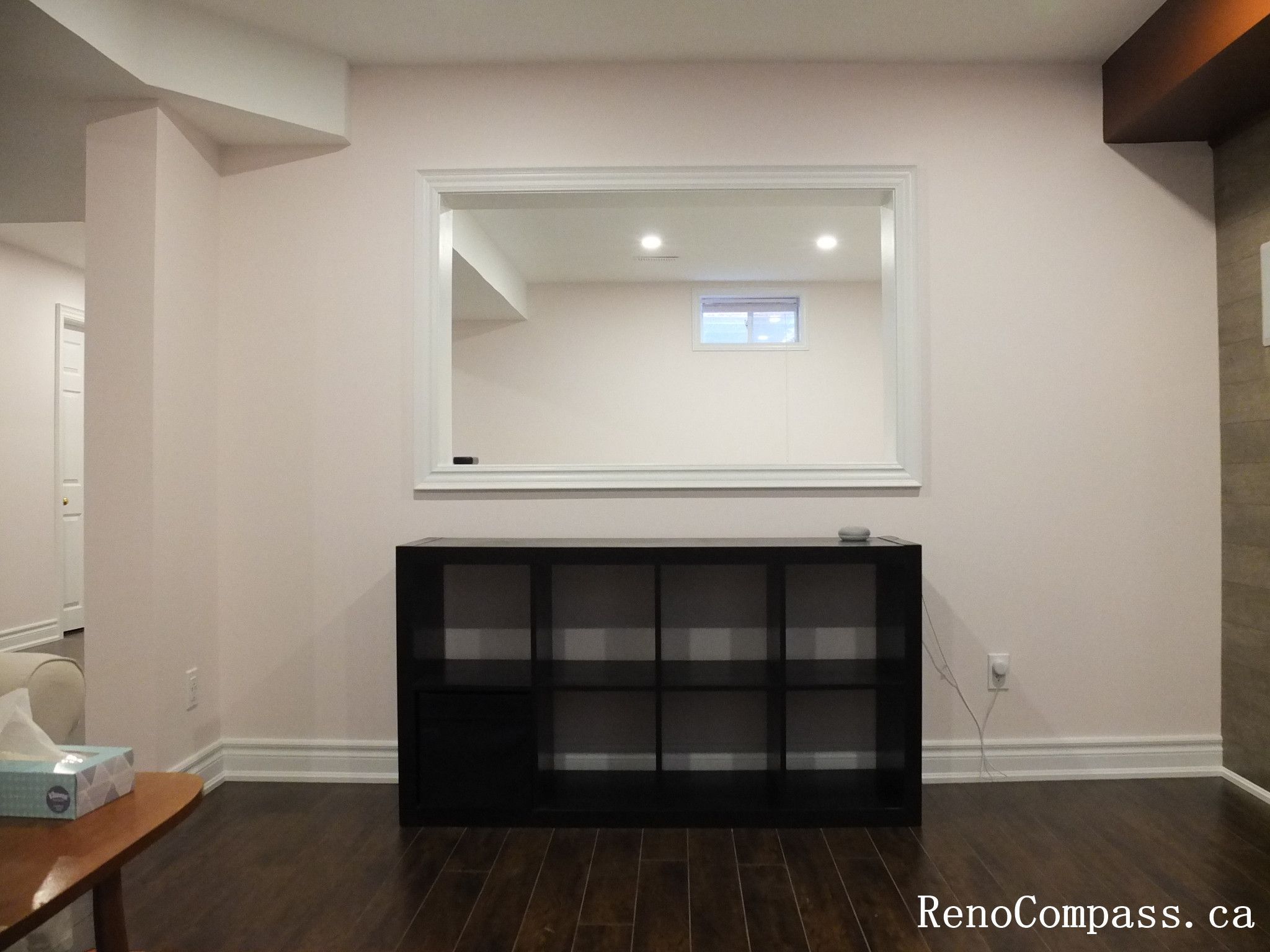 This Newmarket basement renovation features a modern interior opening window that connects different areas of the finished basement while maintaining an open and bright atmosphere. The space includes dark hardwood flooring, clean wall finishes, recessed lighting, and a minimalist storage cabinet that enhances both function and visual balance. The interior pass-through design improves sightlines and creates a more connected layout within the basement living space. Completed by Reno Compass Inc., this project reflects thoughtful basement finishing and practical interior design for modern homes.