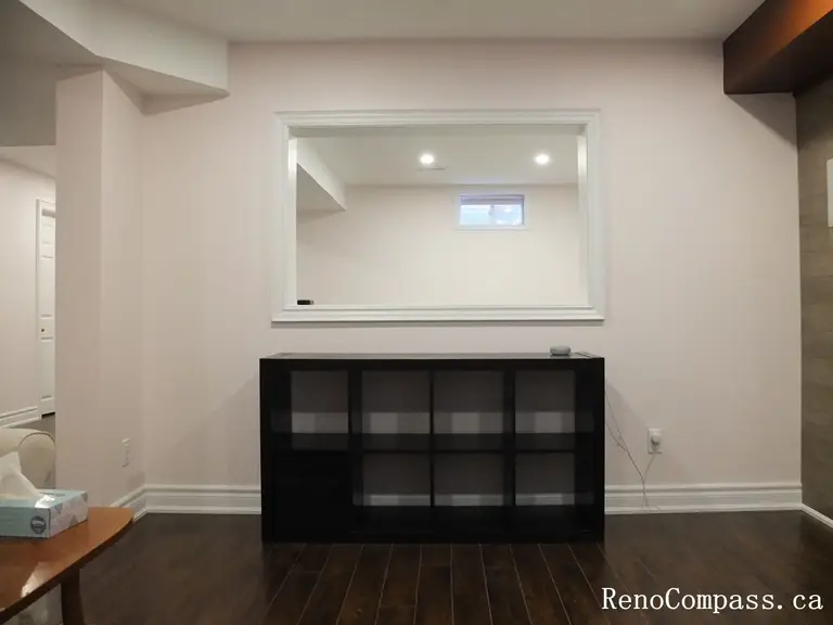 This Newmarket basement renovation features a modern interior opening window that connects different areas of the finished basement while maintaining an open and bright atmosphere. The space includes dark hardwood flooring, clean wall finishes, recessed lighting, and a minimalist storage cabinet that enhances both function and visual balance. The interior pass-through design improves sightlines and creates a more connected layout within the basement living space. Completed by Reno Compass Inc., this project reflects thoughtful basement finishing and practical interior design for modern homes.