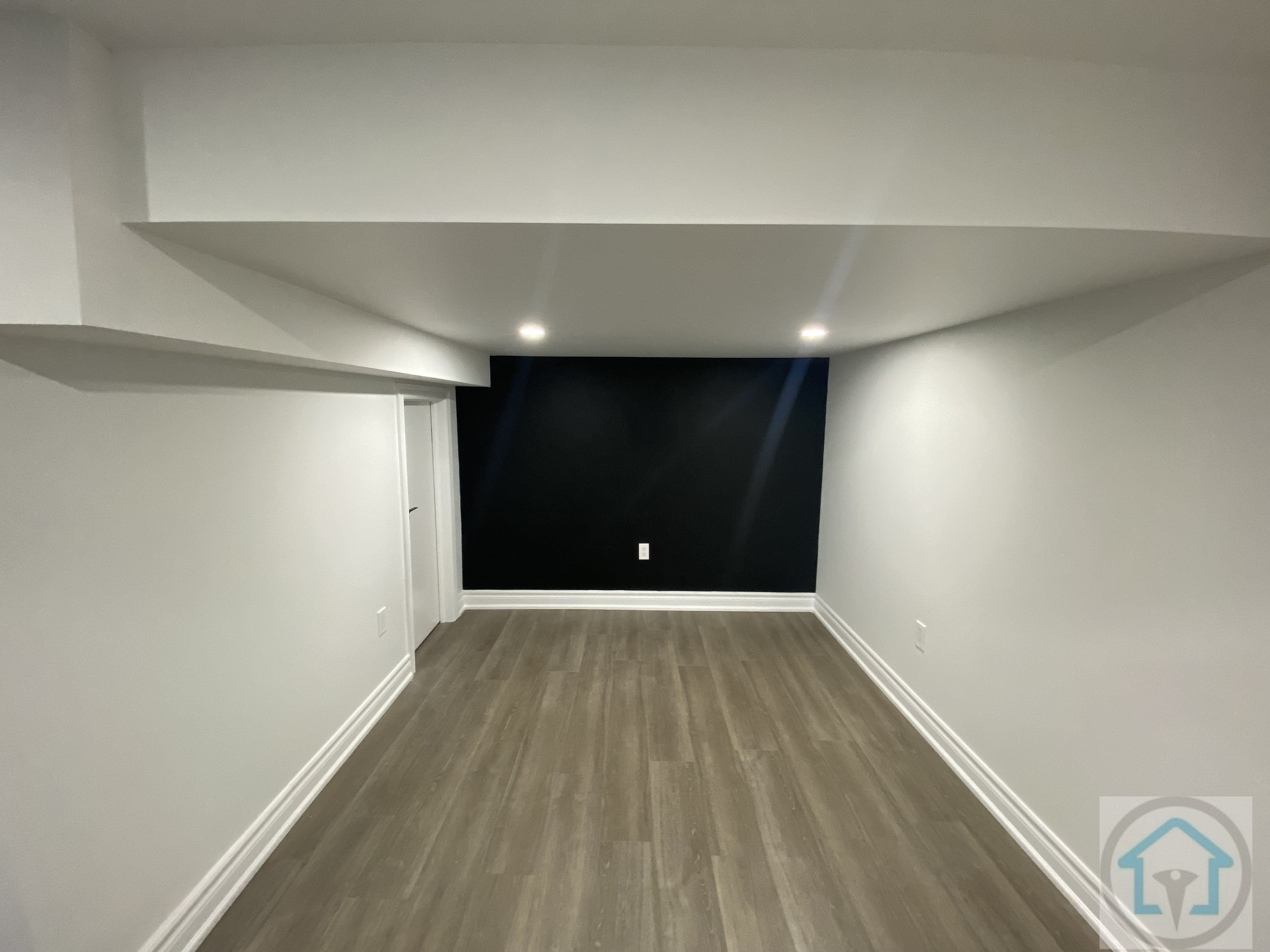 Spacious Aurora basement featuring dark accent wall, recessed lighting, and modern flooring, ideal for a home theater, entertainment, or media room setup. Contractor: Reno Compass Inc.