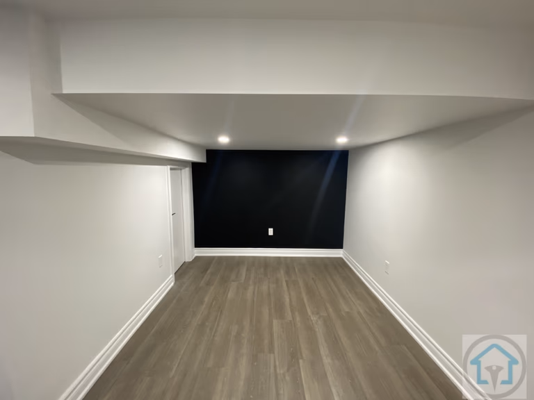 Spacious Aurora basement featuring dark accent wall, recessed lighting, and modern flooring, ideal for a home theater, entertainment, or media room setup. Contractor: Reno Compass Inc.