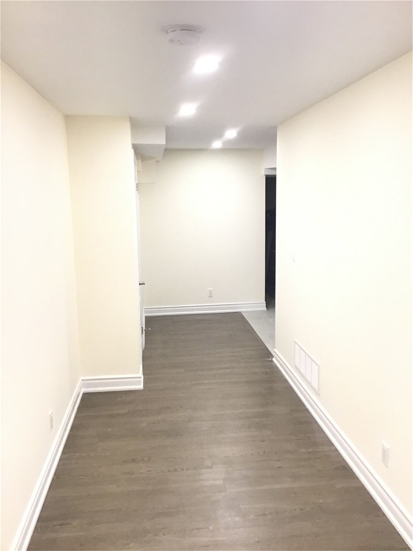 This Mississauga basement renovation features a clean and modern hallway with durable wood-look flooring, smooth painted walls, and recessed pot lights that enhance brightness and visual depth. The layout improves flow and connects different functional areas within the basement.