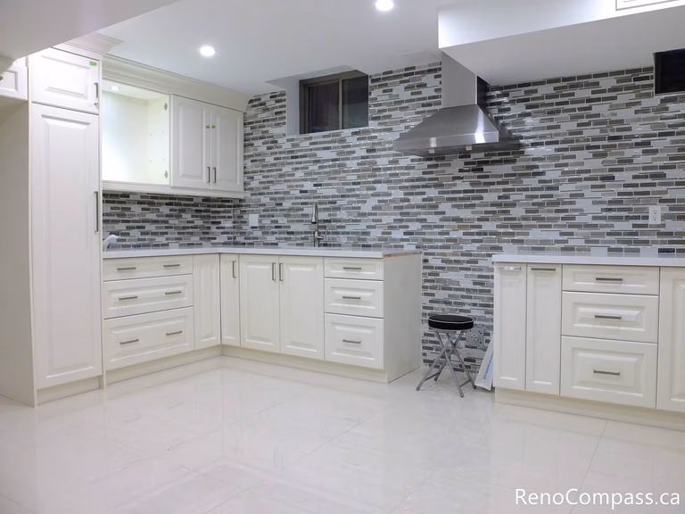 This Markham basement renovation features a bright and functional kitchen with white shaker cabinets, full-height storage, and a modern mosaic tile backsplash. The clean layout, stainless steel range hood, and durable flooring create a stylish and practical secondary kitchen space, ideal for rental or multi-generational living. Completed by a trusted Toronto Renovation Company, Reno Compass Inc.
