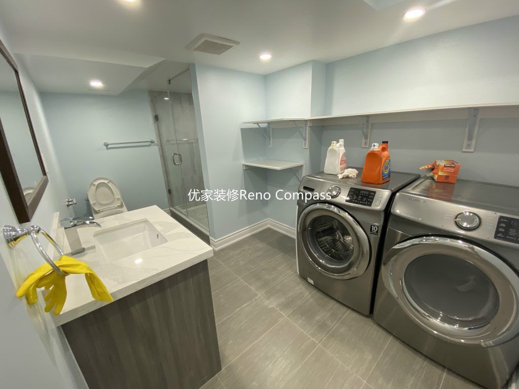 This Aurora basement renovation includes a modern bathroom and laundry area upgrade completed by a professional Toronto renovation company. The space features a sleek vanity with quartz countertop, contemporary tile flooring, glass walk-in shower, and a dedicated washer and dryer setup with custom shelving for efficient storage. Bright LED pot lights and soft neutral tones enhance the clean and functional layout, transforming the basement into a fully equipped and comfortable living space. Contractor: Reno Compass Inc.