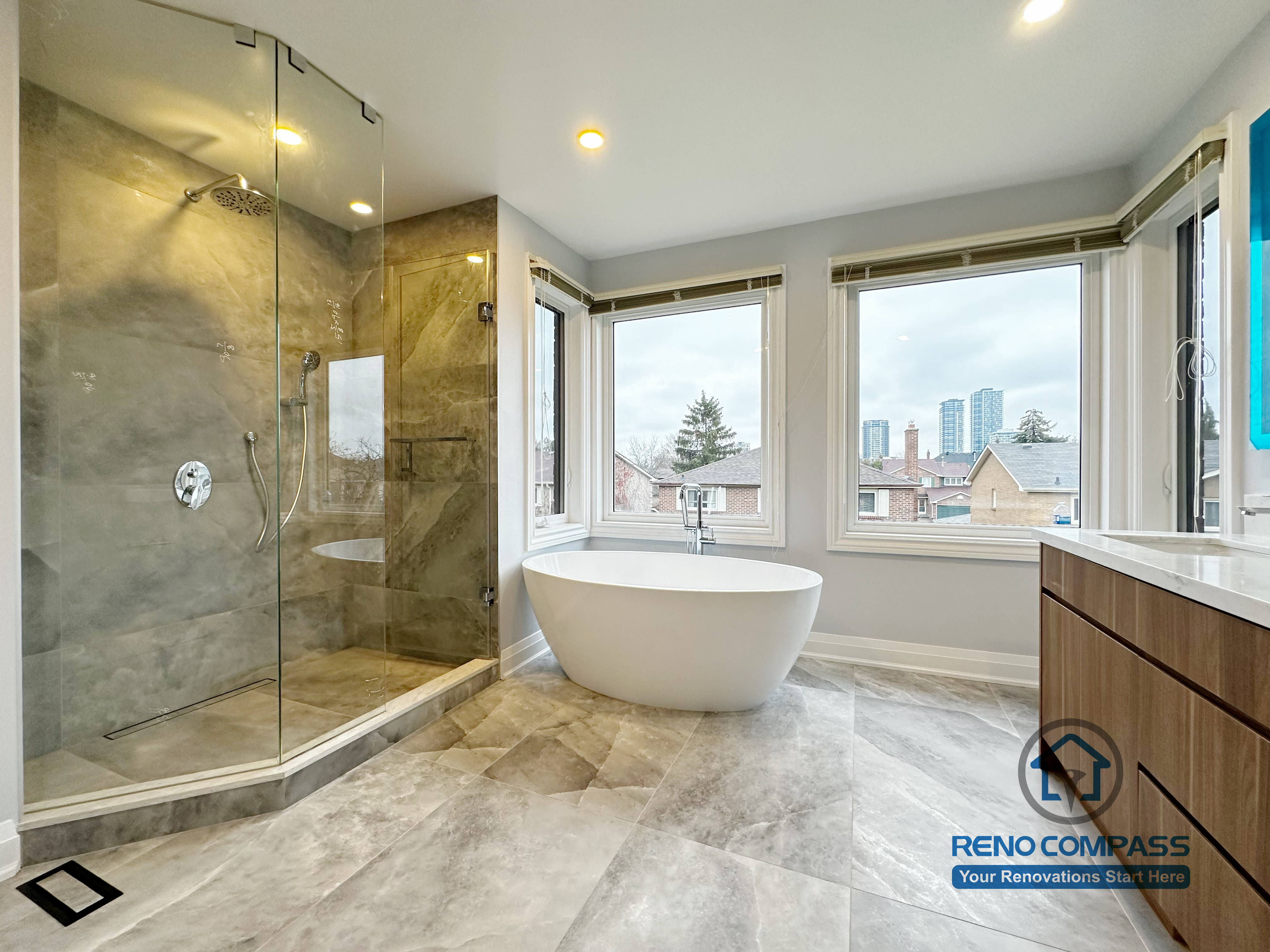 Bathroom renovation in Markham featuring a freestanding soaking tub, frameless glass shower, and large-format tile flooring. Expansive windows enhance natural light, creating a bright, spa-inspired bathroom with a clean and modern layout.