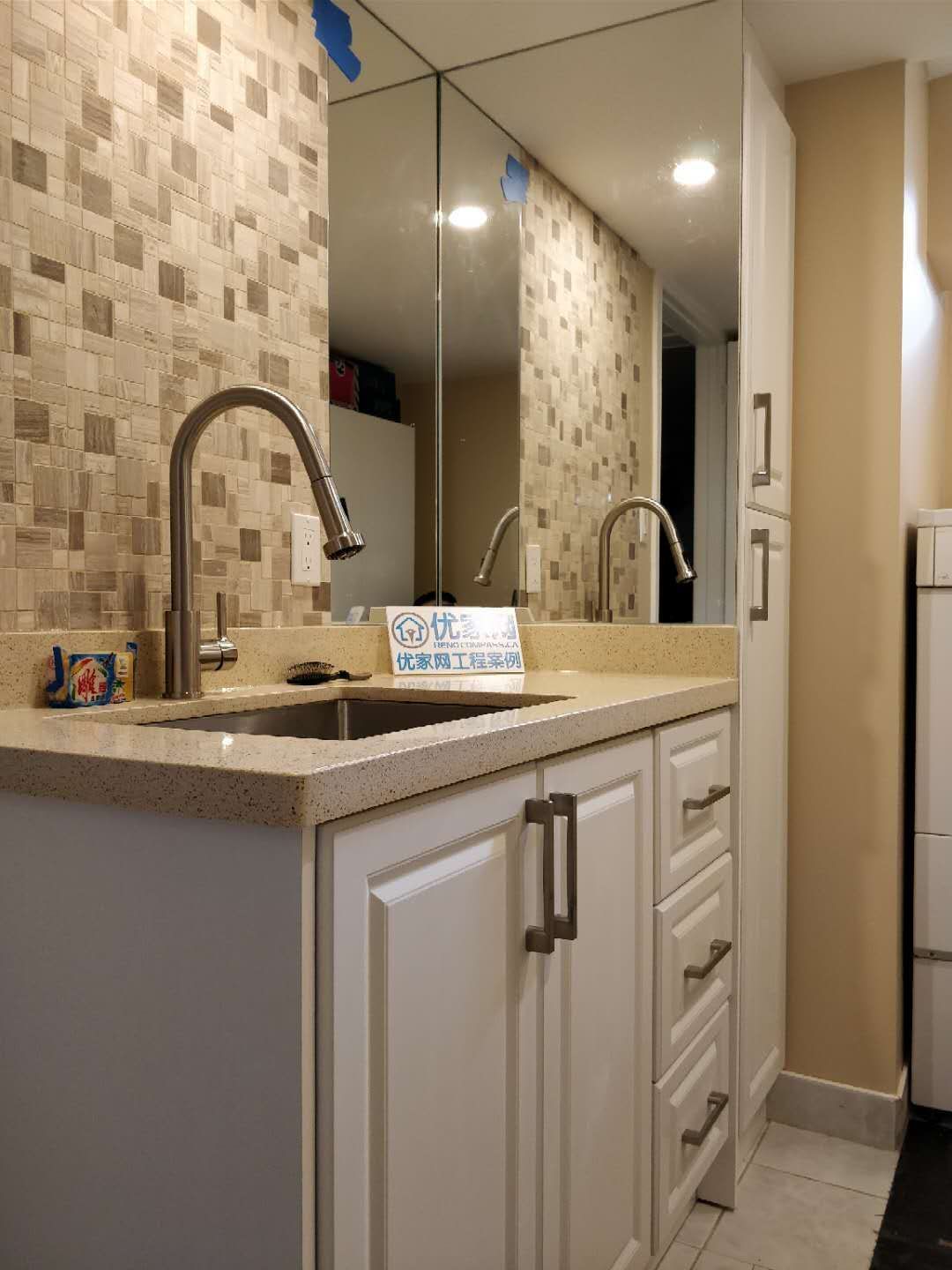 Stylish basement wet bar area completed as part of a Scarborough interior renovation. The design features custom white cabinetry, quartz countertop, modern pull-down faucet, mosaic tile backsplash, and a large wall mirror to enhance light and depth, creating a functional and elegant entertainment space for the home.