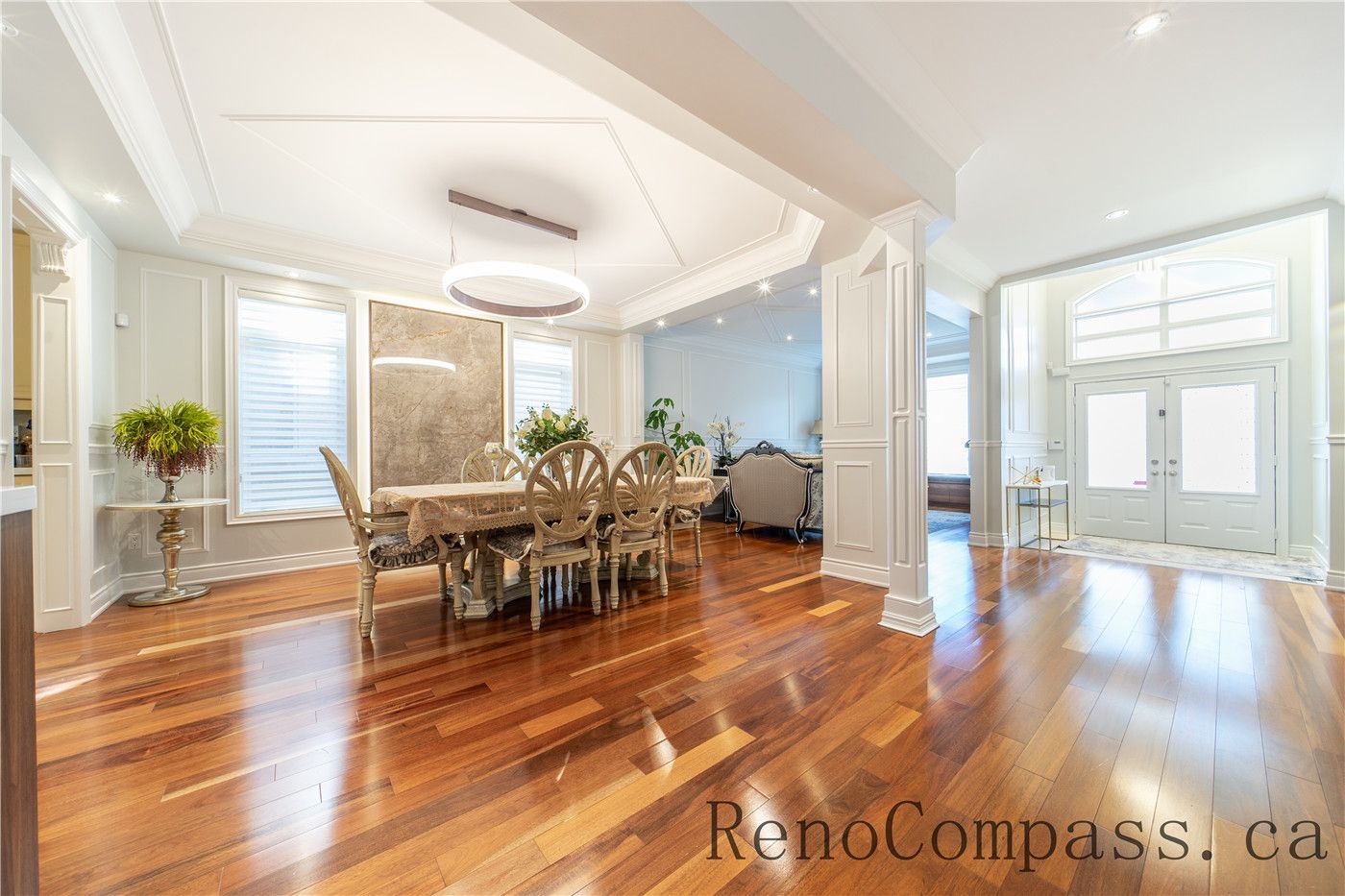 This Richmond Hill entire house interior renovation highlights an elegant open-concept dining and living area featuring rich hardwood flooring, custom ceiling detailing, and decorative columns. Large windows and a bright foyer connection enhance natural light and spatial flow throughout the home. The refined layout and timeless finishes create a warm, luxurious atmosphere, professionally completed by a leading Toronto renovation company focused on quality craftsmanship and modern functionality.