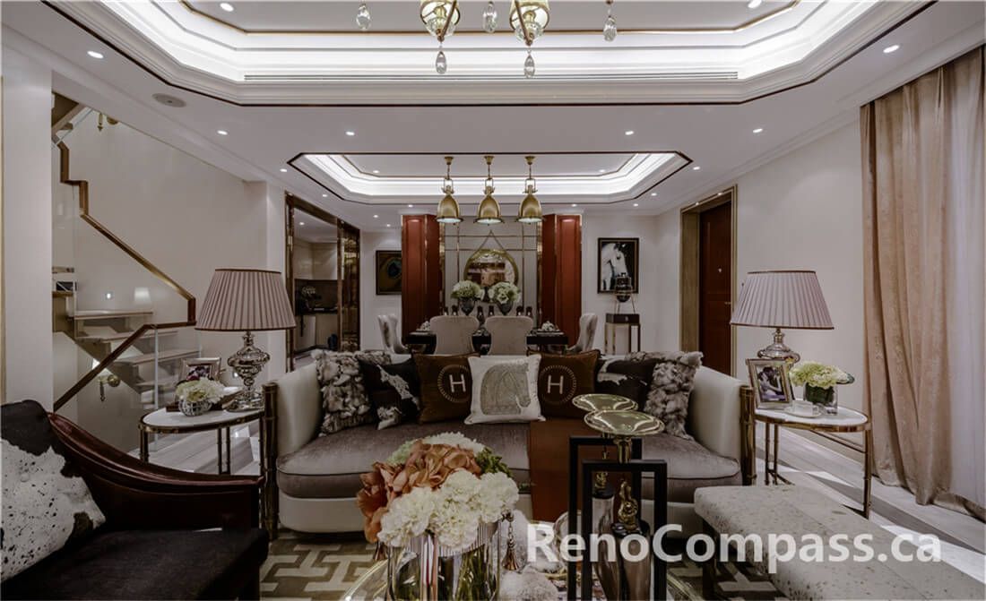 This Toronto interior renovation highlights a sophisticated living room featuring layered tray ceiling detailing, custom lighting design, and a balanced open-concept layout connecting the lounge and dining space. Warm wood accents, marble flooring, and refined décor elements create a luxurious yet welcoming atmosphere. Completed by a trusted Toronto Renovation Company, this project reflects high-end craftsmanship, thoughtful spatial planning, and timeless interior elegance suitable for upscale residential living.