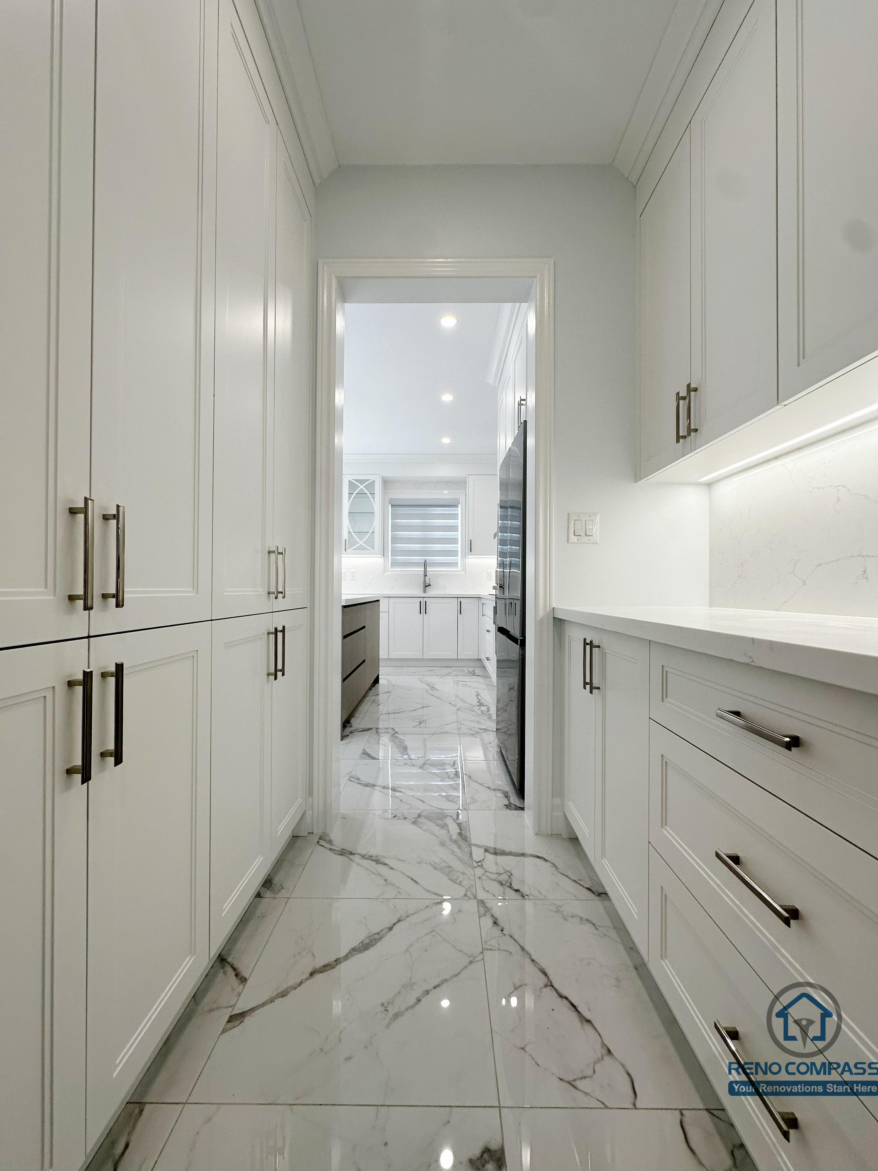 Custom kitchen storage corridor featuring full-height cabinetry, integrated drawers, and marble-look flooring, creating a seamless transition between prep space and main kitchen while maximizing everyday storage.