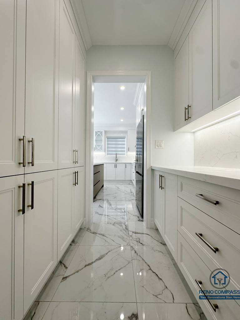 Custom kitchen storage corridor featuring full-height cabinetry, integrated drawers, and marble-look flooring, creating a seamless transition between prep space and main kitchen while maximizing everyday storage.