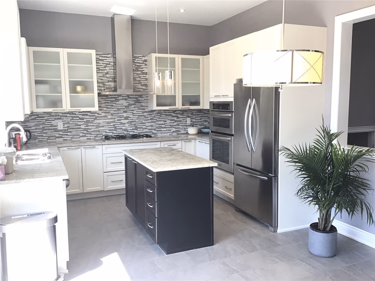 This Markham full home renovation features a bright and modern kitchen with a functional center island, stainless steel appliances, and a stylish mosaic tile backsplash. The combination of white cabinetry and dark island creates visual contrast, while the open layout enhances both workflow and space efficiency. Completed by a trusted Toronto Renovation Company, this kitchen design blends practicality with contemporary elegance.