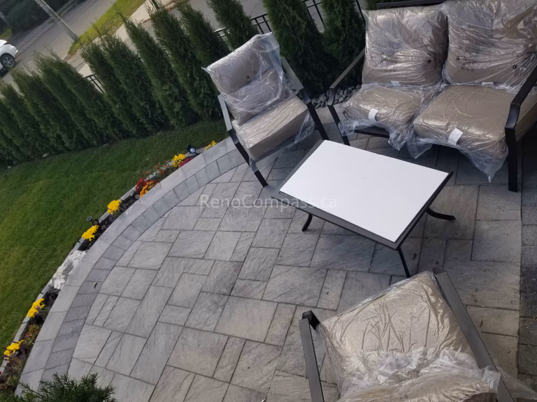 This Toronto landscaping renovation features a beautifully designed raised stone patio with a curved layout, creating a comfortable outdoor seating and relaxation space. The project includes decorative garden beds with vibrant seasonal flowers, natural stone accents, river rock drainage detail, and modern landscape lighting. Surrounded by privacy hedges and fresh lawn, this professionally completed Toronto backyard landscaping upgrade enhances both functionality and curb appeal while providing a stylish outdoor living environment.