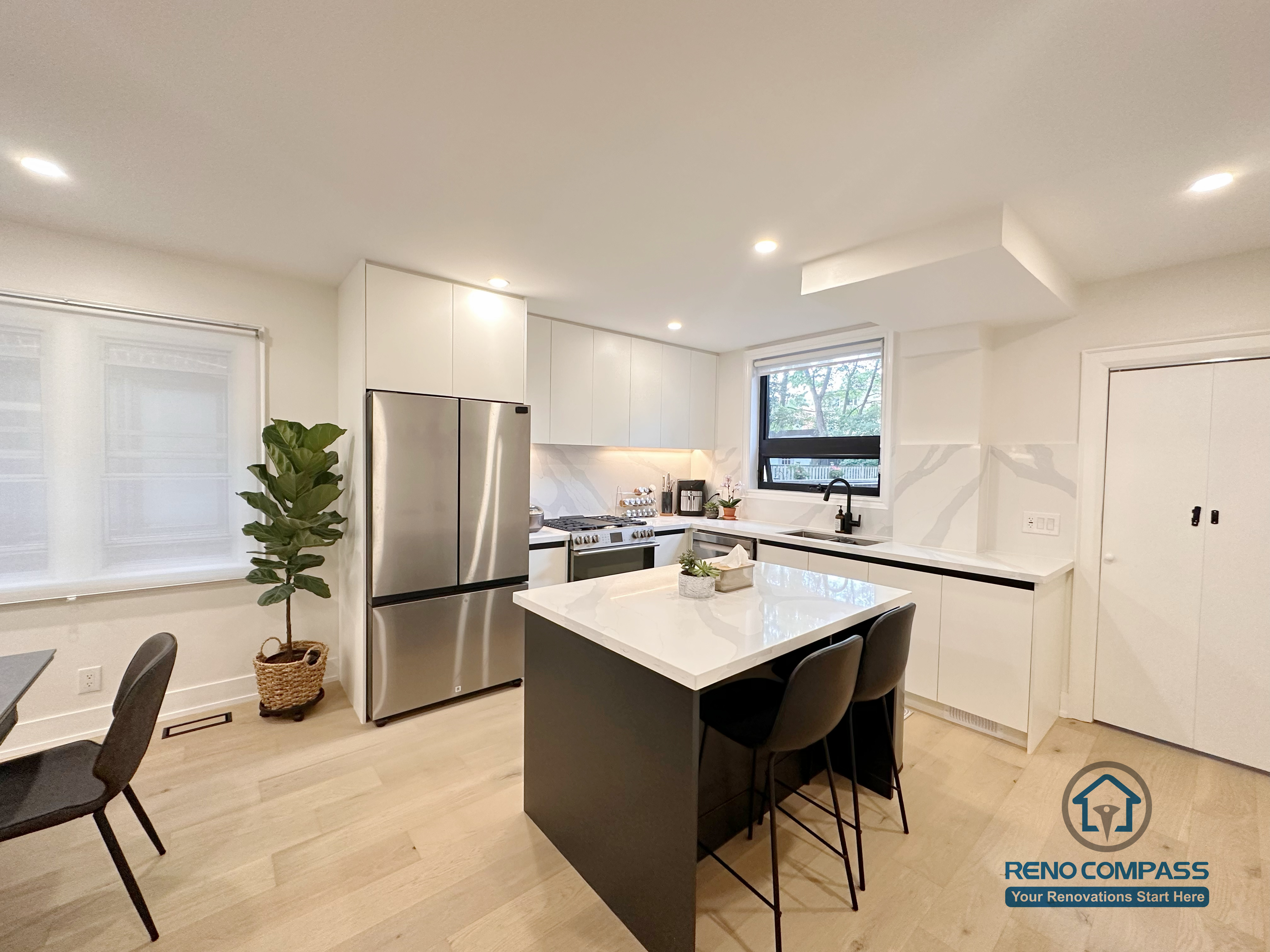 This Toronto interior renovation showcases a modern white kitchen featuring flat-panel cabinetry, a quartz waterfall island, stainless steel appliances, and recessed ceiling lighting. The clean lines and functional layout highlight contemporary kitchen design and quality workmanship delivered by a professional Toronto renovation company.