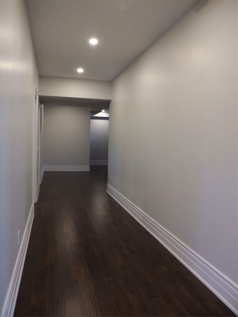 This Richmond Hill basement renovation showcases a clean and modern hallway design featuring dark hardwood flooring, smooth neutral walls, and energy-efficient recessed pot lights. The long corridor enhances flow and connectivity between basement spaces while maintaining a bright and elegant atmosphere. Professionally finished to deliver durability, comfort, and a seamless contemporary look for the home.