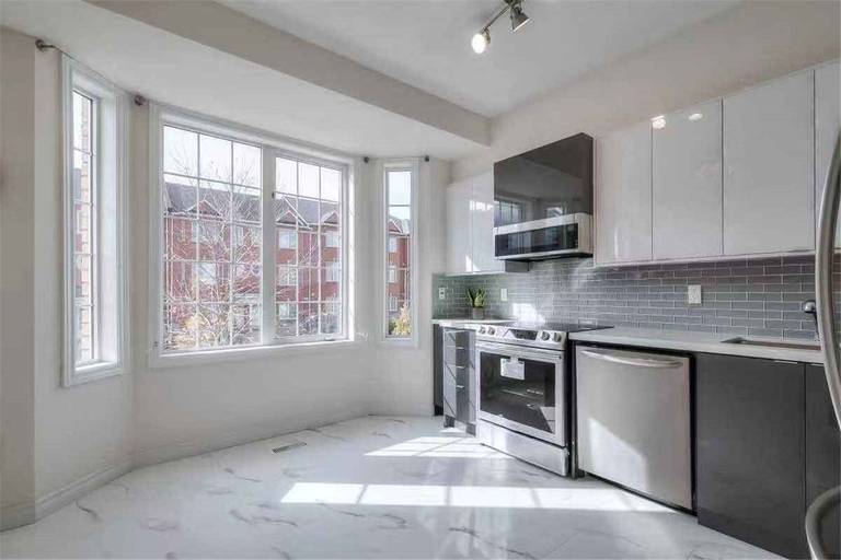 This Thornhill interior renovation showcases a bright and modern kitchen featuring glossy white cabinetry, stainless steel appliances, grey tile backsplash, and elegant marble-style flooring. Large bay windows bring in abundant natural light, enhancing the open and spacious feel of the home. Completed by a professional Toronto renovation team, this upgrade delivers a clean, contemporary interior designed for both comfort and functionality.