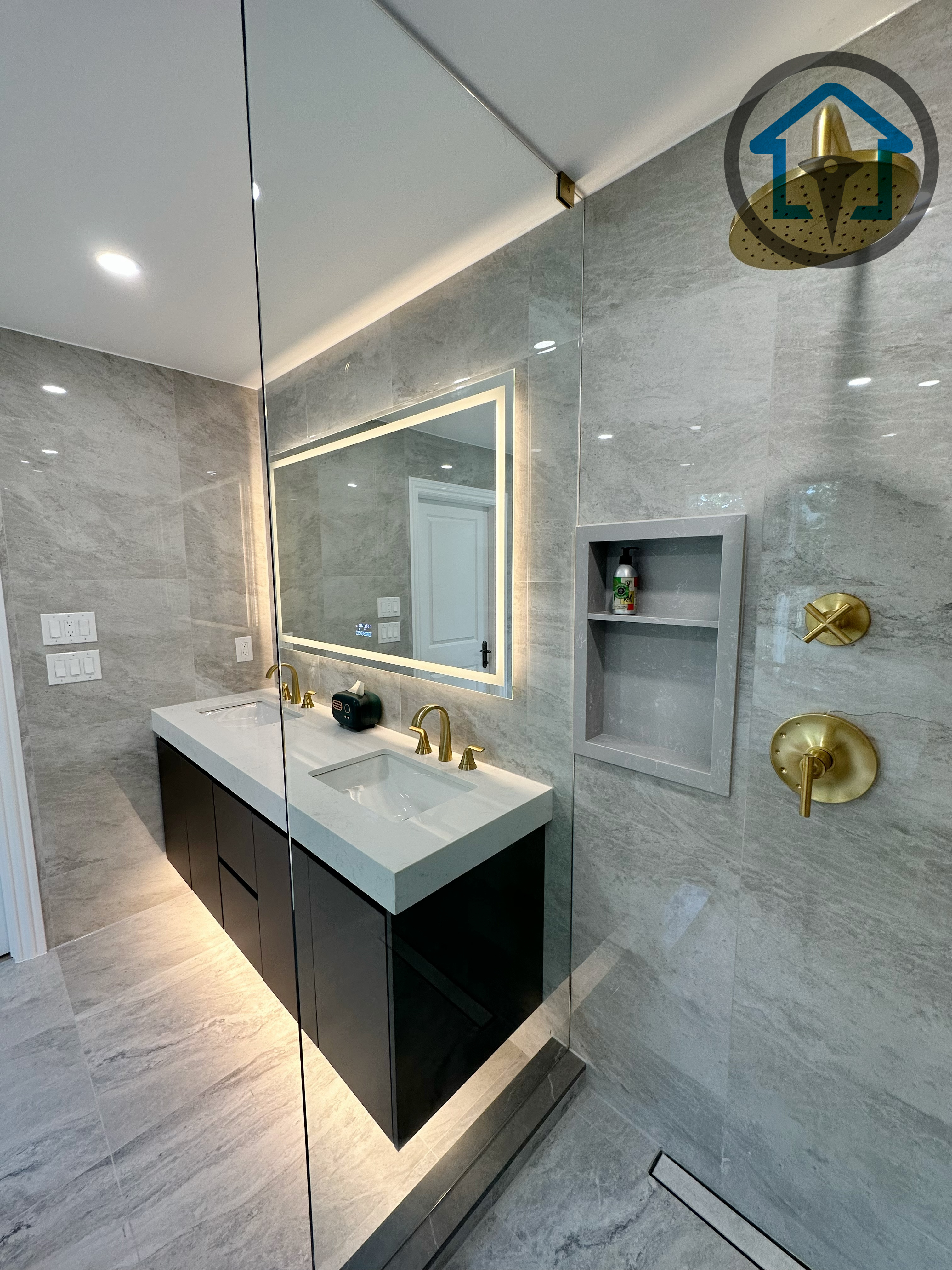 Modern bathroom completed as part of a North York interior renovation, featuring a custom double vanity, integrated LED mirror, large-format marble-look tile, and a frameless glass shower with brushed gold fixtures. The layout emphasizes clean lines, moisture-resistant materials, and a balanced mix of luxury and everyday functionality, completed by a professional Toronto renovation company.