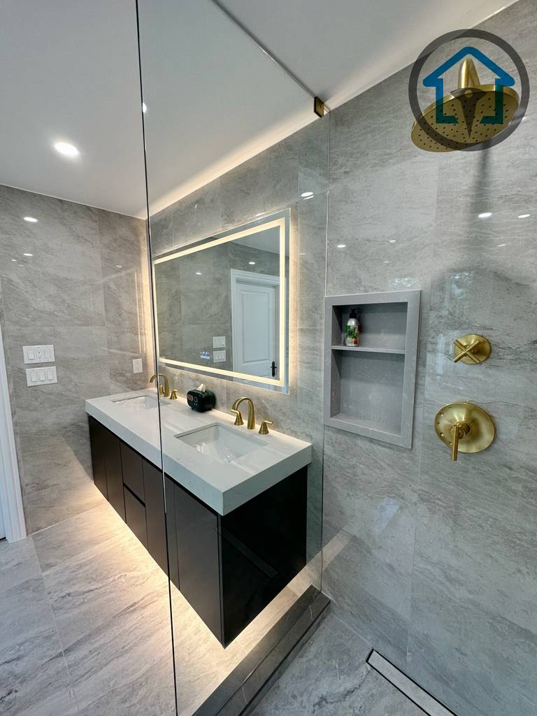 Modern bathroom completed as part of a North York interior renovation, featuring a custom double vanity, integrated LED mirror, large-format marble-look tile, and a frameless glass shower with brushed gold fixtures. The layout emphasizes clean lines, moisture-resistant materials, and a balanced mix of luxury and everyday functionality, completed by a professional Toronto renovation company.