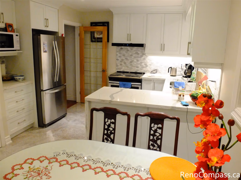 This North York kitchen remodel highlights a functional and stylish layout featuring premium stainless steel appliances, including a French door refrigerator and modern range hood. The bright space is accented by LED under-cabinet lighting and a beautiful textured hexagon tile backsplash.