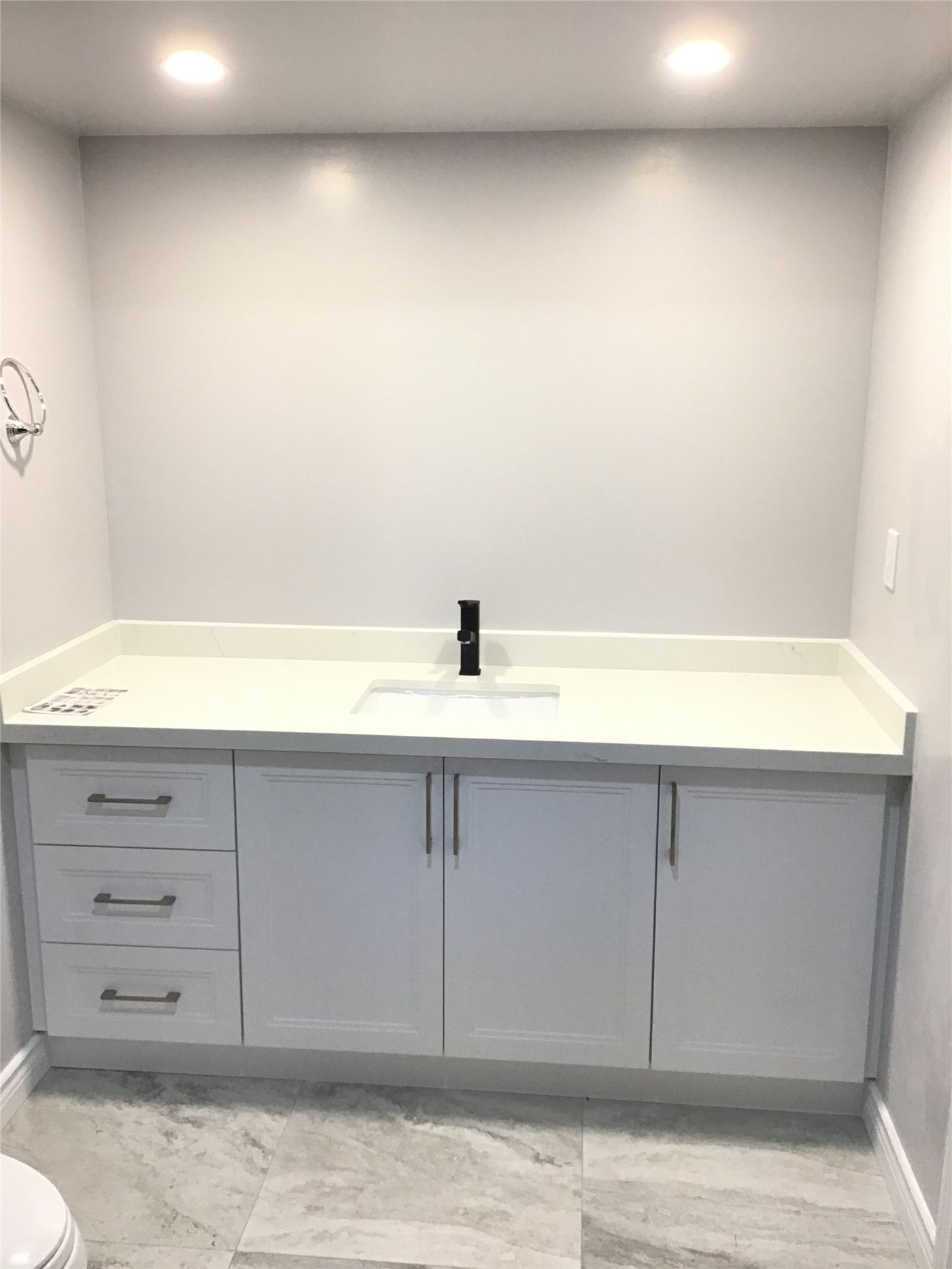 Aurora basement bathroom renovation featuring a custom white vanity with quartz countertop, integrated sink, and matte black faucet for a sleek contemporary look. Large-format marble-style floor tiles enhance durability and visual elegance. Completed by an experienced Toronto renovation company with precise installation and attention to clean, modern finishes.