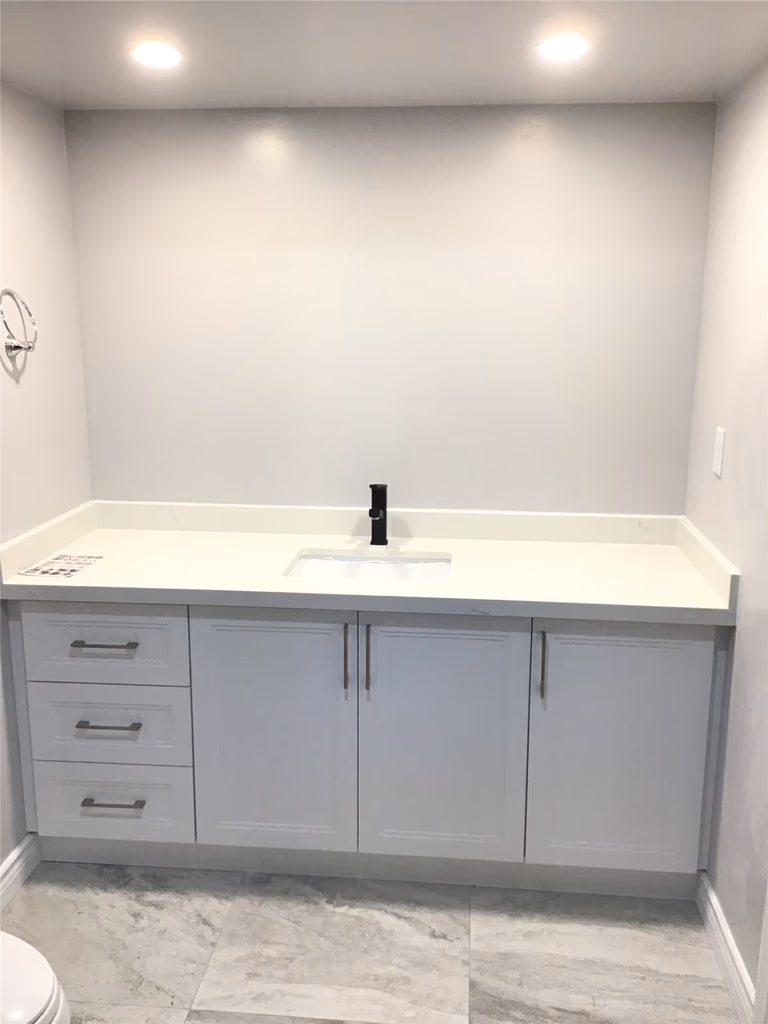 Aurora basement bathroom renovation featuring a custom white vanity with quartz countertop, integrated sink, and matte black faucet for a sleek contemporary look. Large-format marble-style floor tiles enhance durability and visual elegance. Completed by an experienced Toronto renovation company with precise installation and attention to clean, modern finishes.