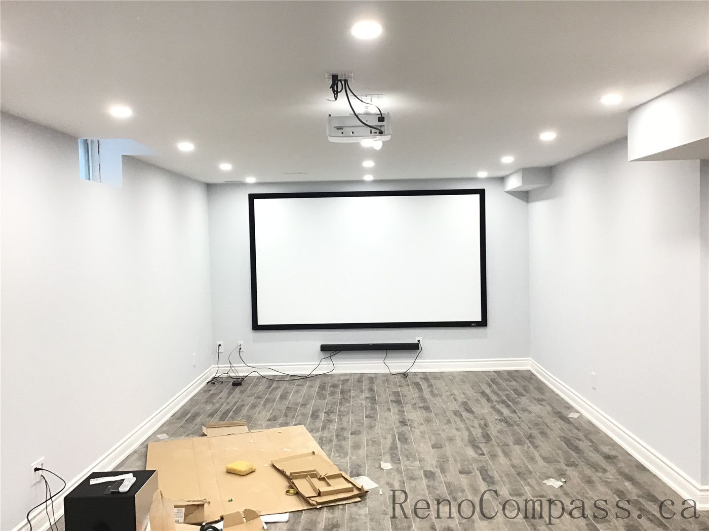Newly finished basement home theater in Richmond Hill featuring a large wall-mounted projector screen, ceiling-mounted projector setup, recessed pot lights, and durable vinyl plank flooring. This entertainment-focused basement renovation creates a comfortable and modern media space completed by a reliable Toronto Renovation Company.
