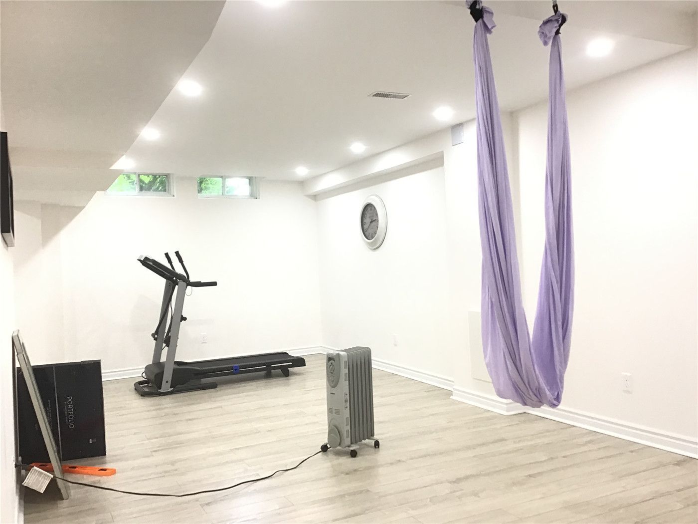 This Aurora basement renovation features a dedicated home gym and wellness area with an open and minimalist layout. The space includes a treadmill, aerial yoga setup, and wide plank flooring, enhanced by recessed ceiling lights for a bright and comfortable workout environment.