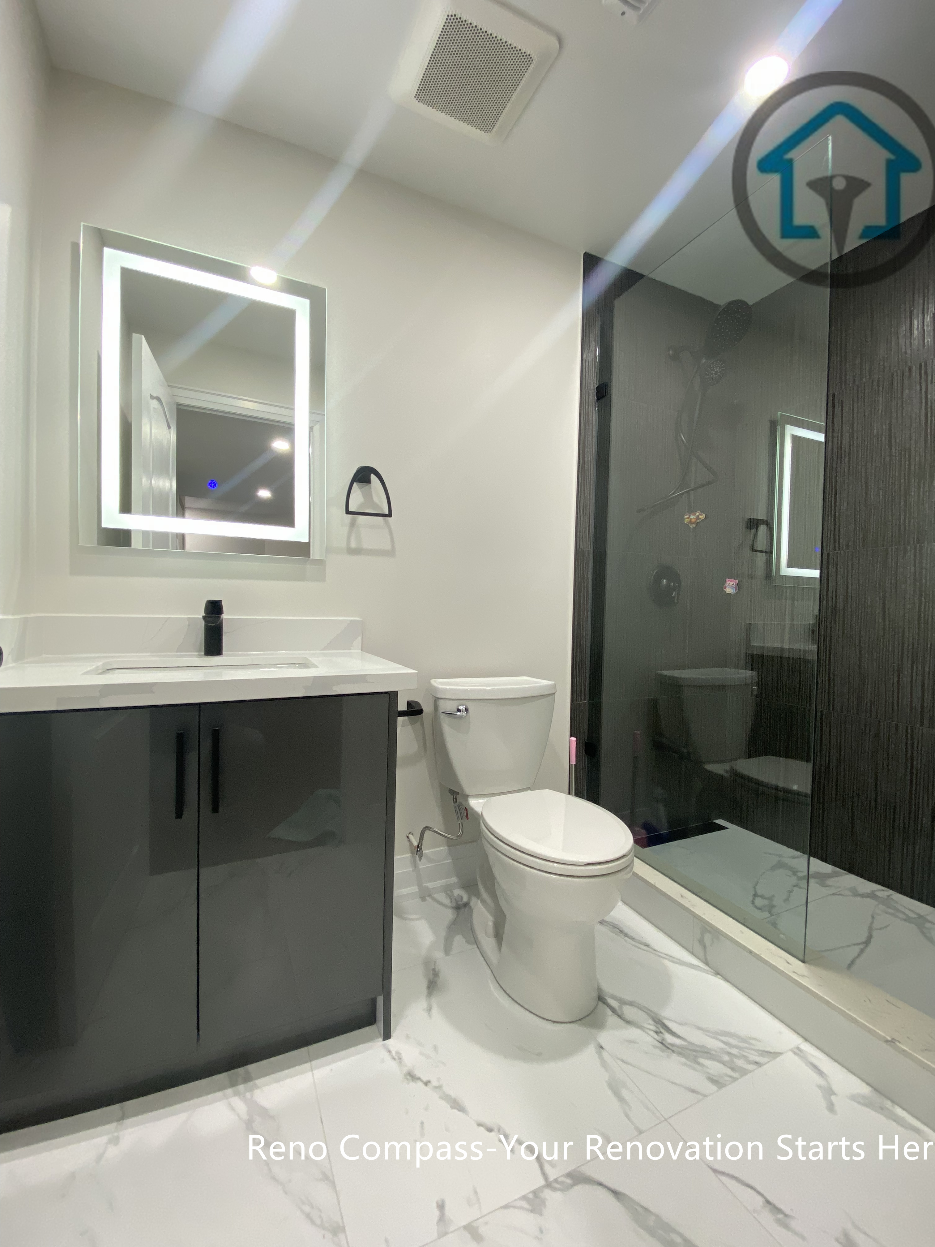 This Stouffville basement bathroom renovation highlights a frameless glass shower, large-format wall tiles, marble-look flooring, LED mirror, and modern vanity with matte black fixtures. The layout maximizes space efficiency while maintaining a clean, contemporary aesthetic, completed by Reno Compass Inc.