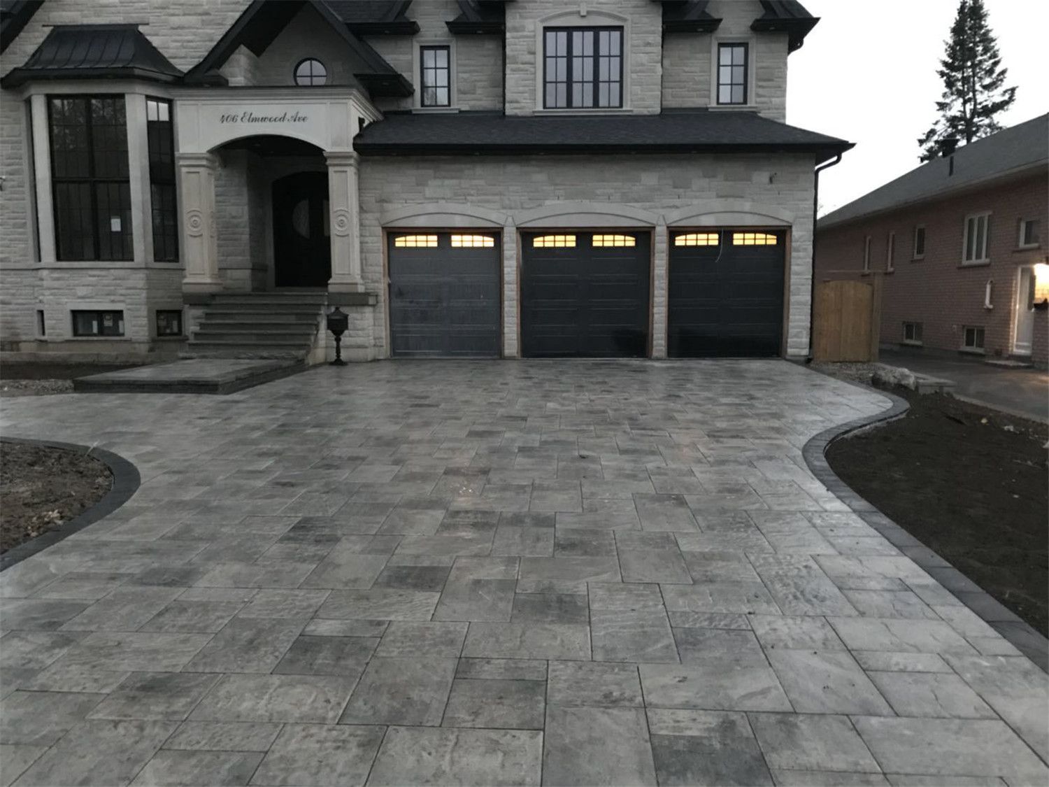 Luxury home front yard landscaping project in Toronto featuring large-format interlocking driveway stones, curved driveway layout, and elegant entrance design that enhances curb appeal and complements the modern residential architecture.