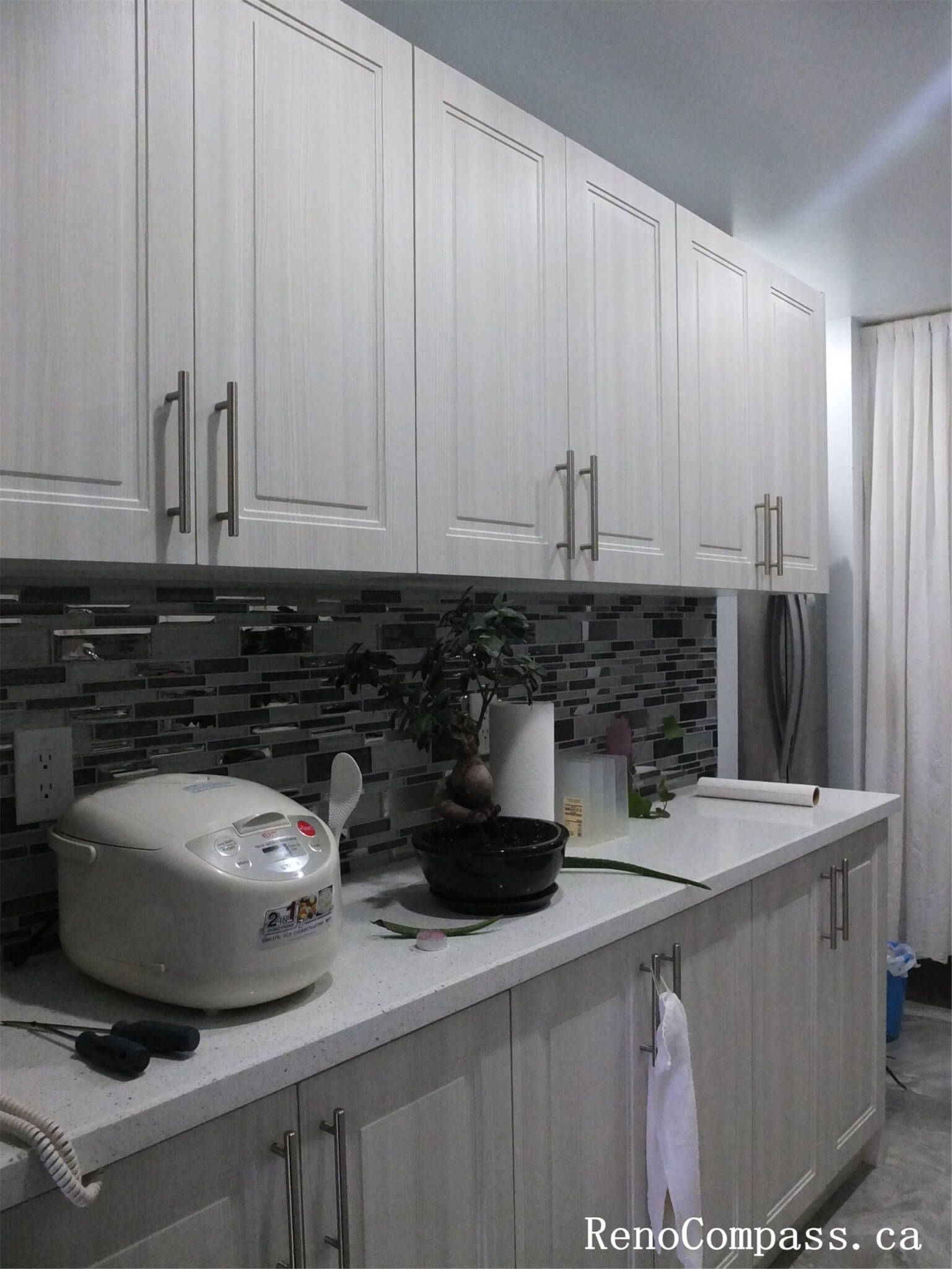This North York interior renovation highlights a streamlined kitchen design featuring full-height shaker-style cabinetry, quartz countertop surfaces, and a modern mosaic tile backsplash. The continuous cabinet layout maximizes vertical storage while maintaining a clean and cohesive visual flow, making the narrow kitchen space feel more organized, functional, and bright for everyday living in Toronto homes.
