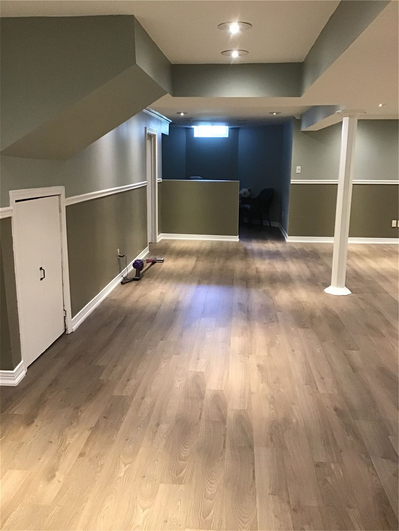 A complete basement transformation showcasing seamless flooring, two-tone wall paint with elegant trim, and clever under-stair storage solutions. Expert interior renovation services in the Markham area.