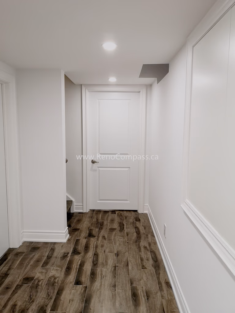 This Vaughan basement renovation features a clean and modern hallway design with durable wood-style flooring, smooth white walls, and recessed ceiling lighting for a bright and welcoming atmosphere. The upgraded basement corridor enhances overall flow and accessibility while maintaining a contemporary finish throughout the space. Completed by Reno Compass Inc., this renovation showcases quality craftsmanship and thoughtful design, creating a polished and functional basement living environment that complements the entire home renovation.